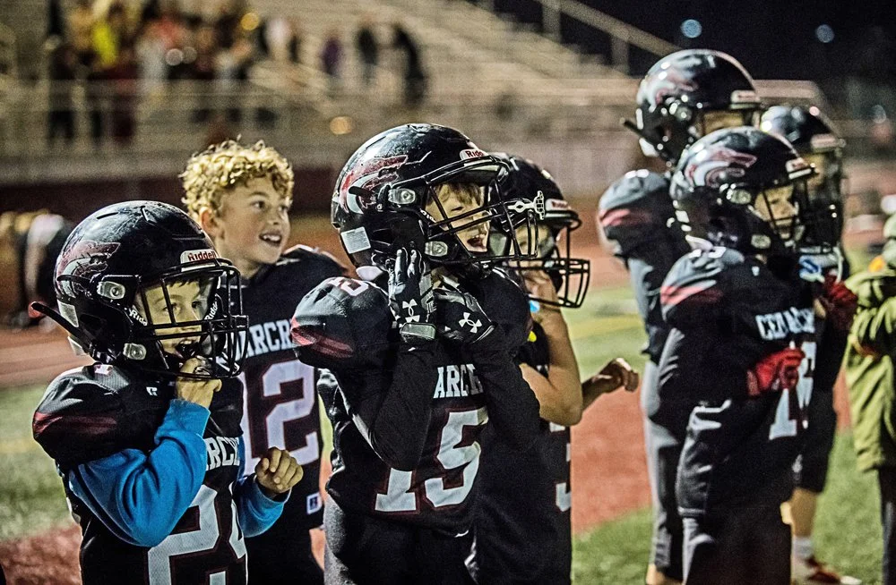 Young Jr. Red Wolves football players in black uniforms preparing for play on a field at night.