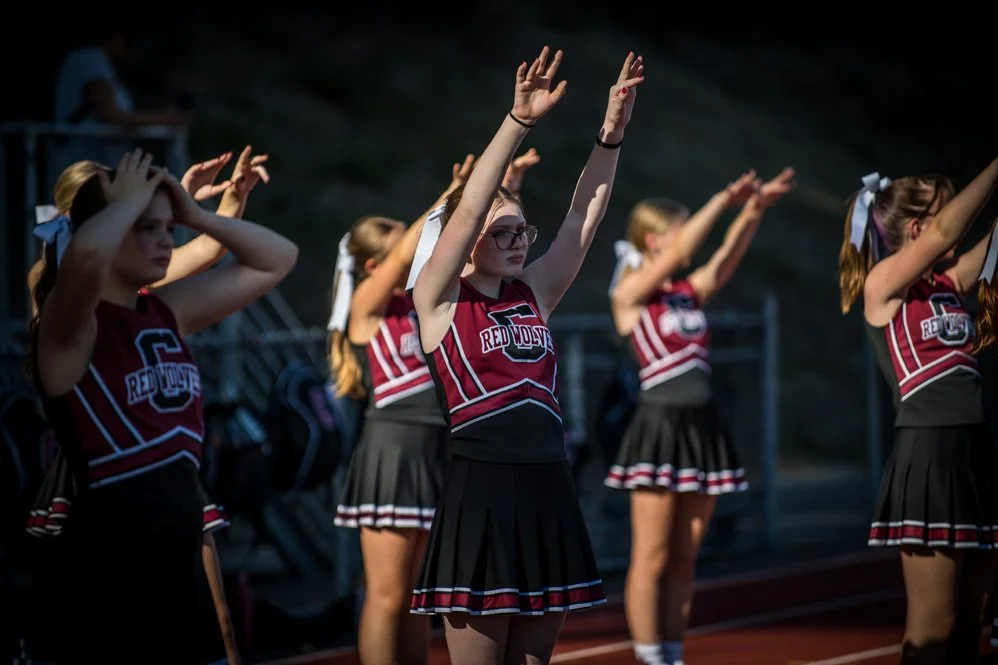 Cheerleaders in red, black, and white uniforms cheer on their team from the sidelines.