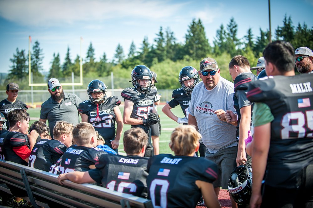 Football team and coaches gathered on a field with coaches giving instructions to young players.