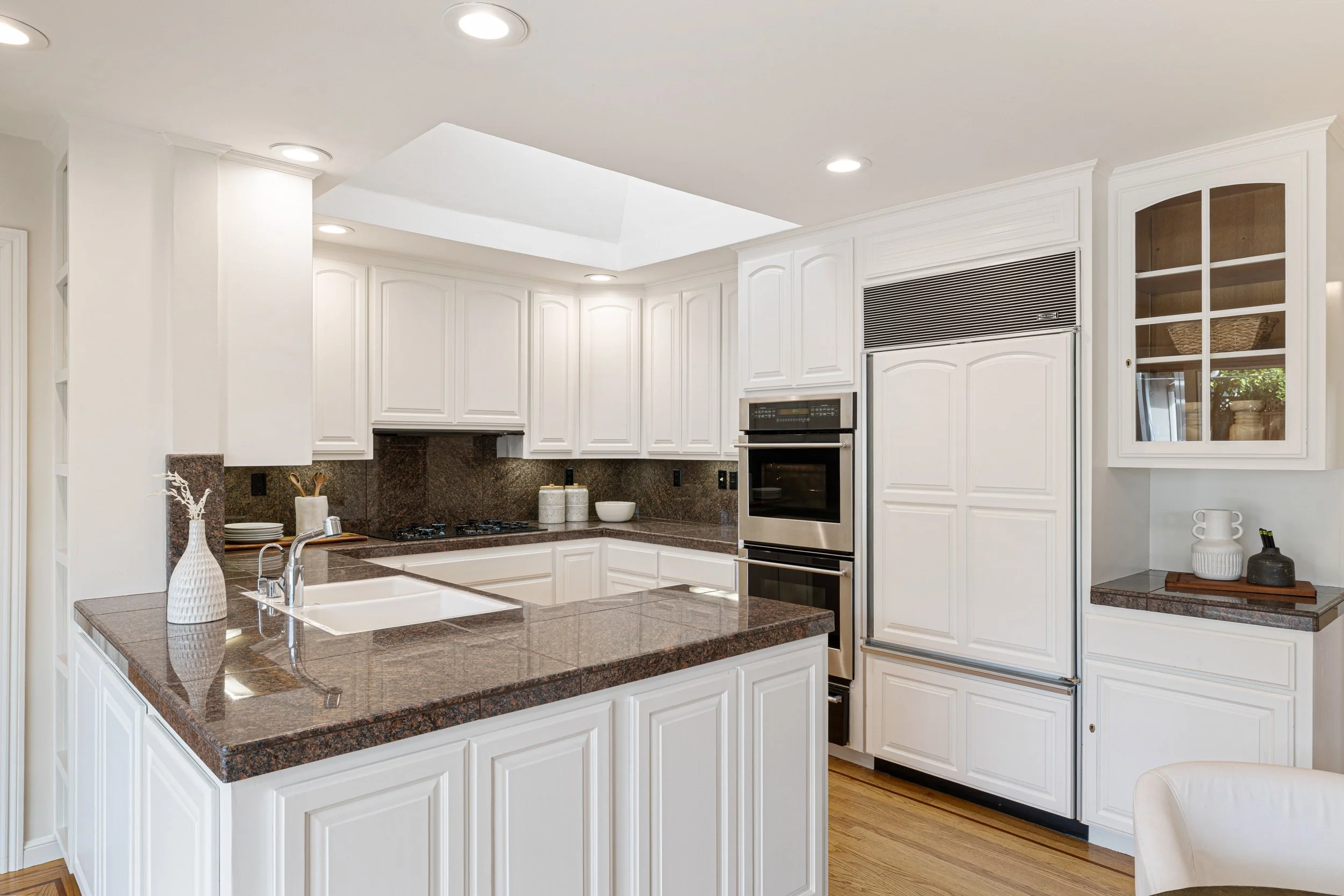 Kitchen with white cabinets, brown granite countertops, stainless steel oven, and refrigerator, with a central island and decorative items on the counters.