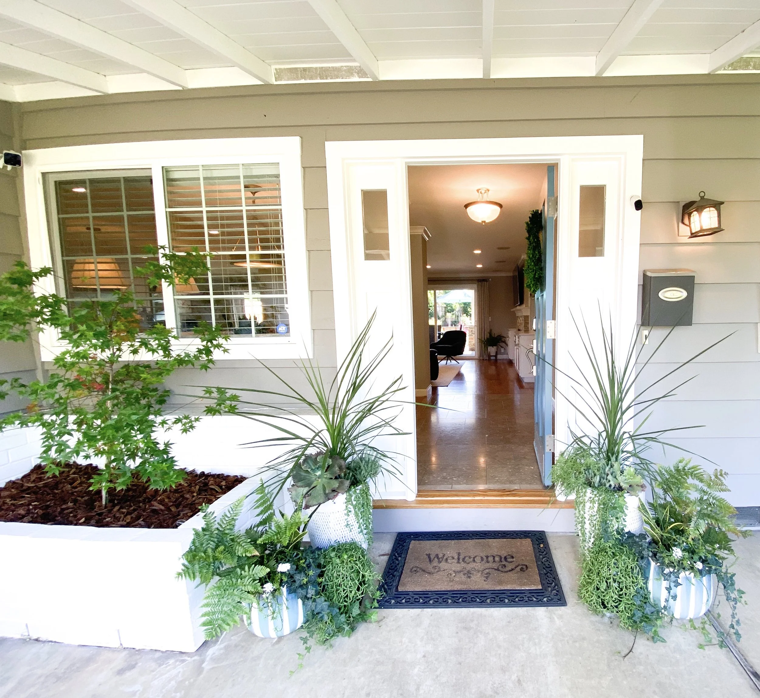 Front porch with potted plants and welcome mat leading into the house.