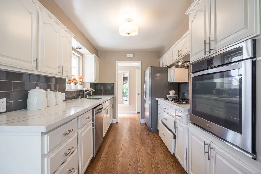 Modern kitchen with white cabinets, stainless steel appliances, gray subway tile backsplash, and hardwood flooring.