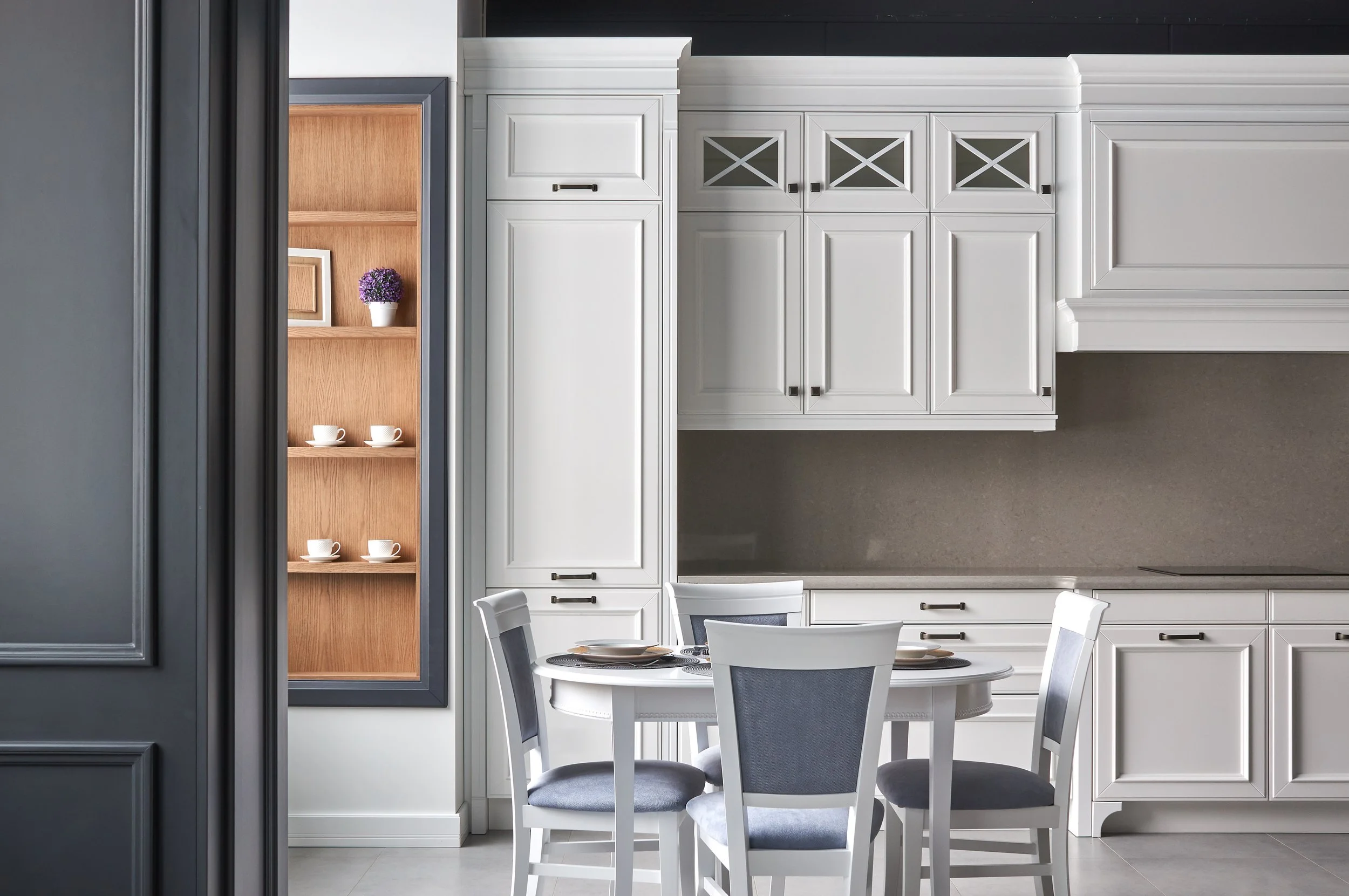 A dining area in a kitchen with a round white table set with plates and four chairs, and white cabinets on the wall.