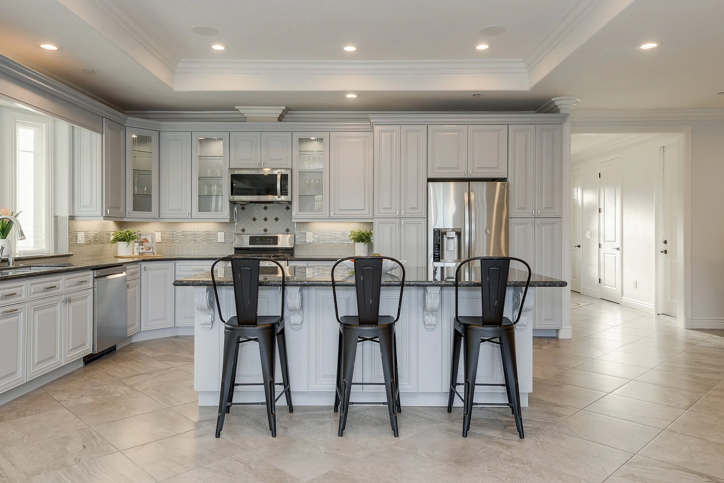 Modern kitchen with white cabinets, granite countertops, stainless steel appliances, and a central island with three black chairs.
