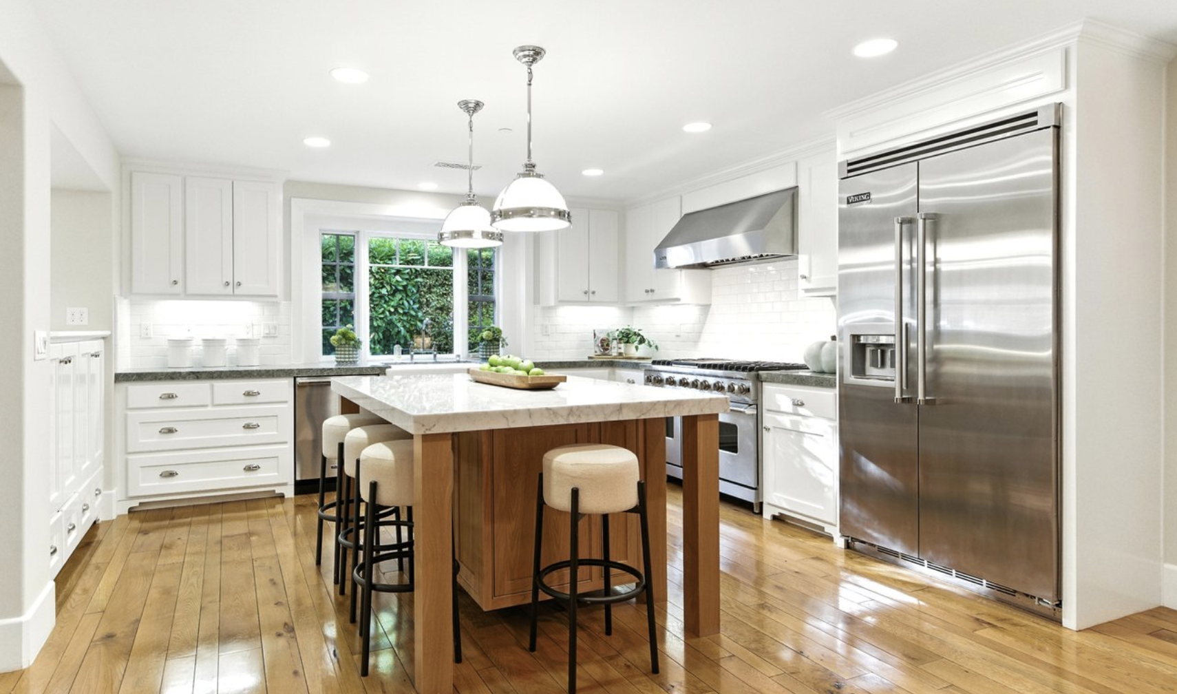 Bright modern kitchen with white cabinets, stainless steel appliances, a wooden island, and hardwood floors.