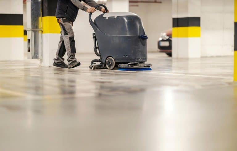 A person operating a floor cleaning machine in an indoor parking garage.