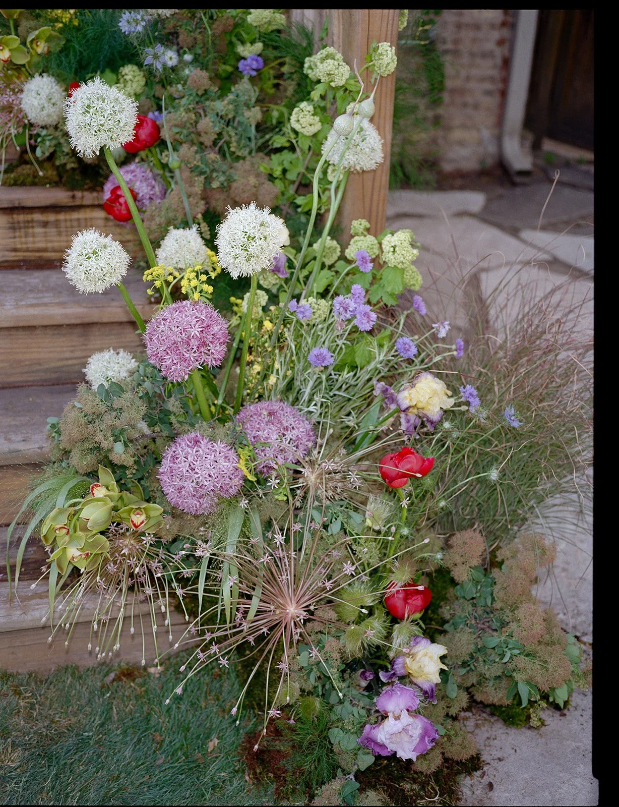 A colorful flower arrangement with various types of flowers including white, purple, yellow, and red blossoms, placed against a wooden structure outdoors.