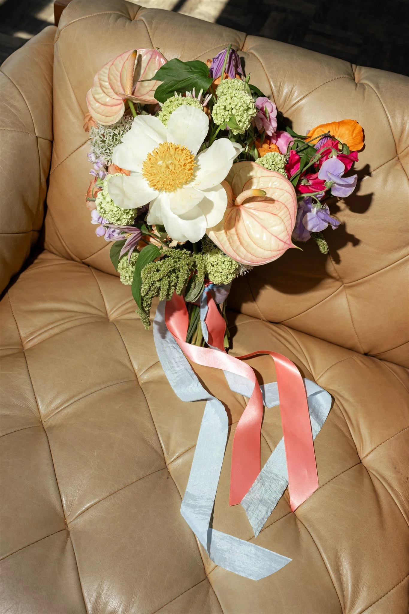 A bouquet of various colorful flowers placed on a beige leather tufted sofa.