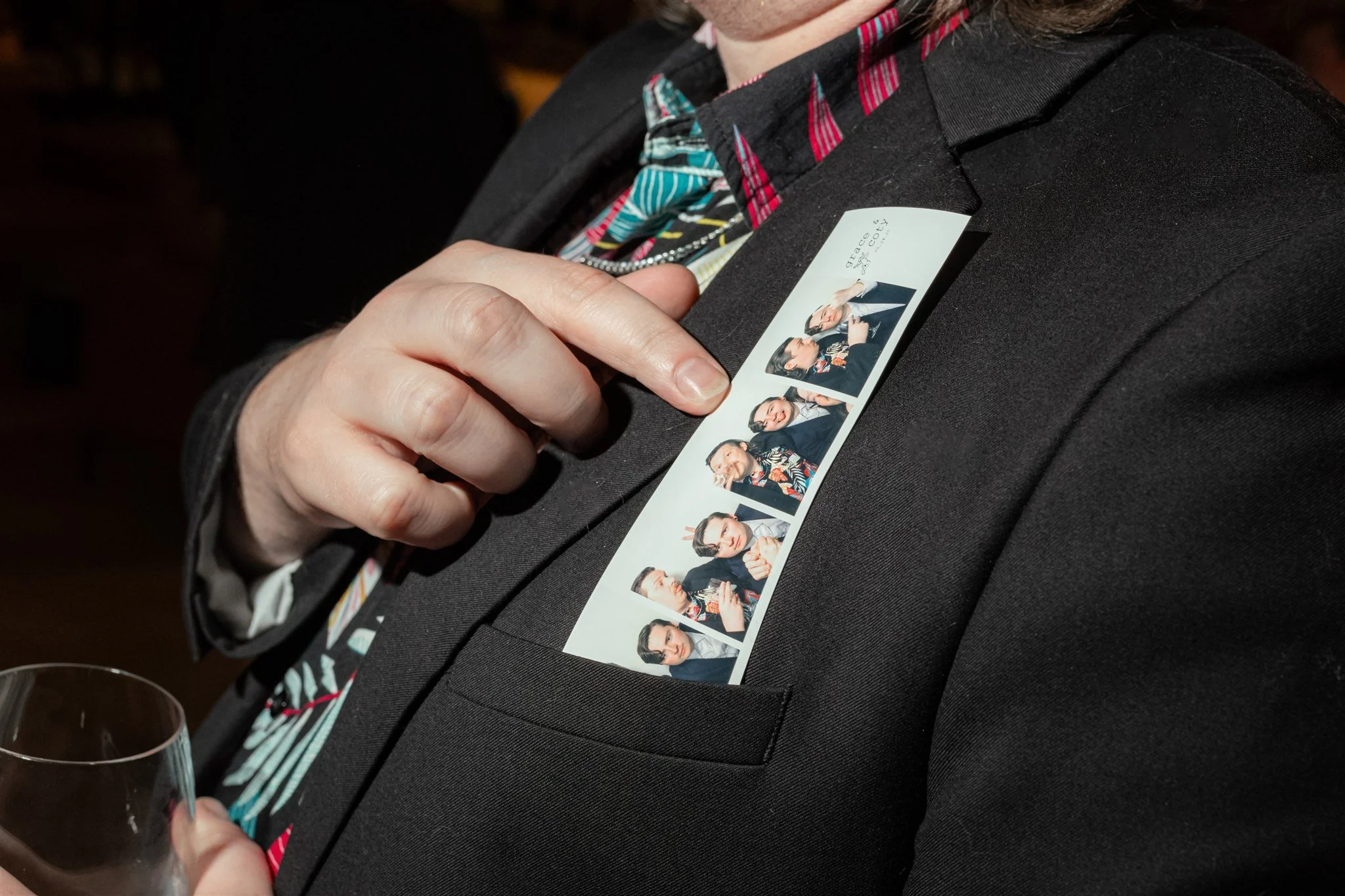 A person in a black suit jacket holding a contact sheet with multiple photos of themselves, wearing different outfits and making various facial expressions, attached to the jacket.