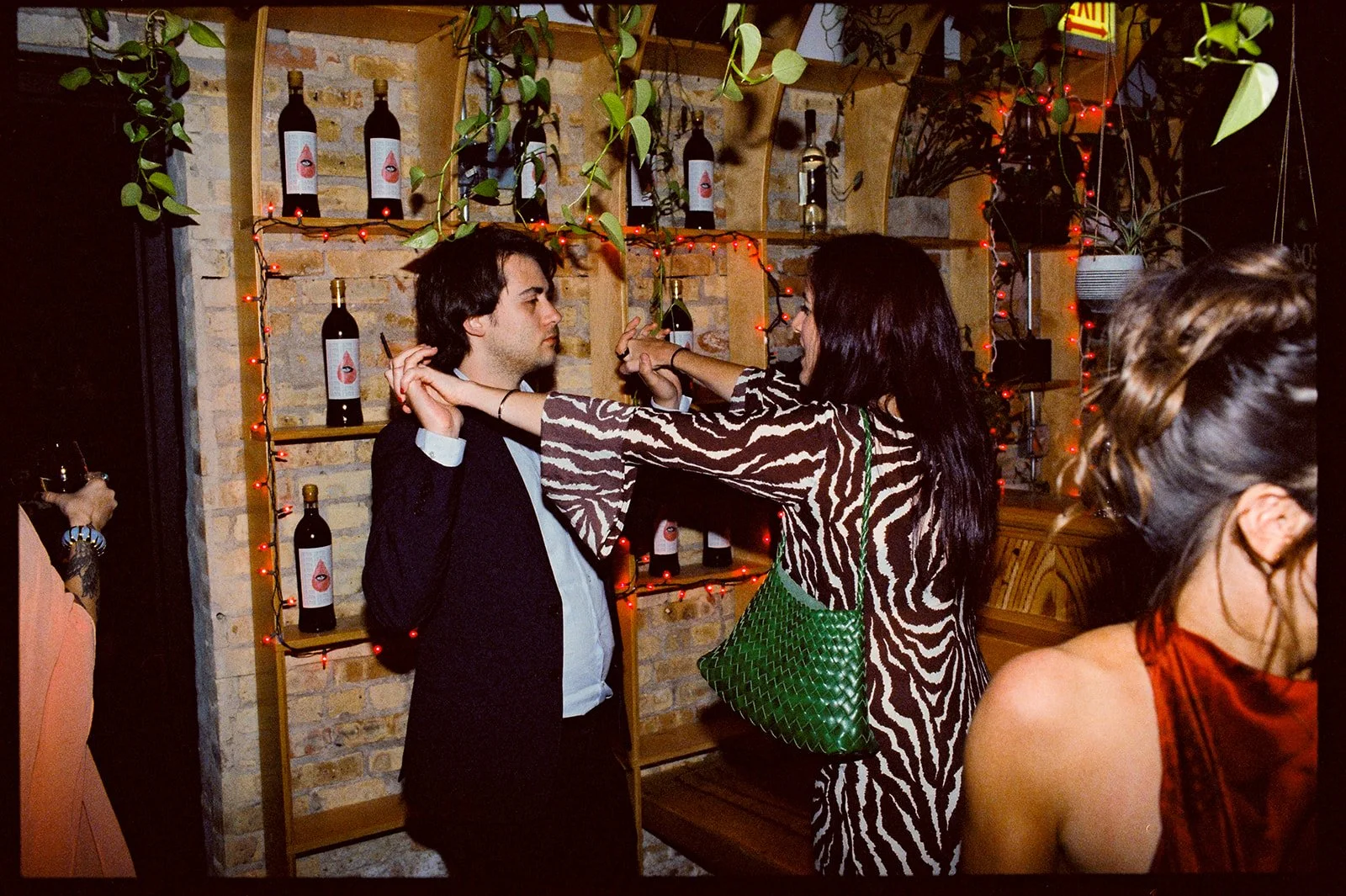 People in a bar or restaurant socializing, with string lights and wine bottles in the background.