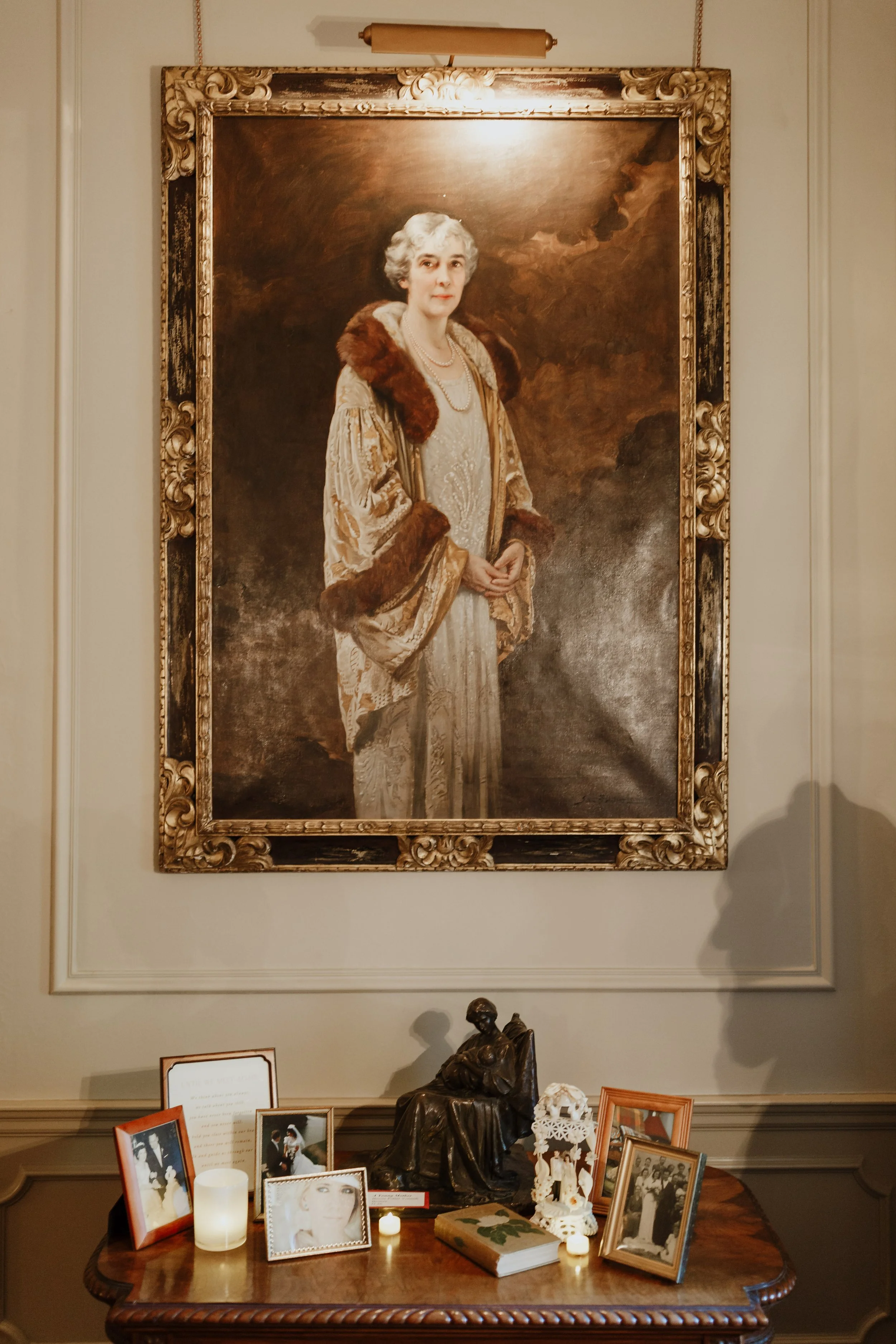 A large portrait of Queen Elizabeth II hanging on a wall above a table with framed photographs, candles, and decorative items.