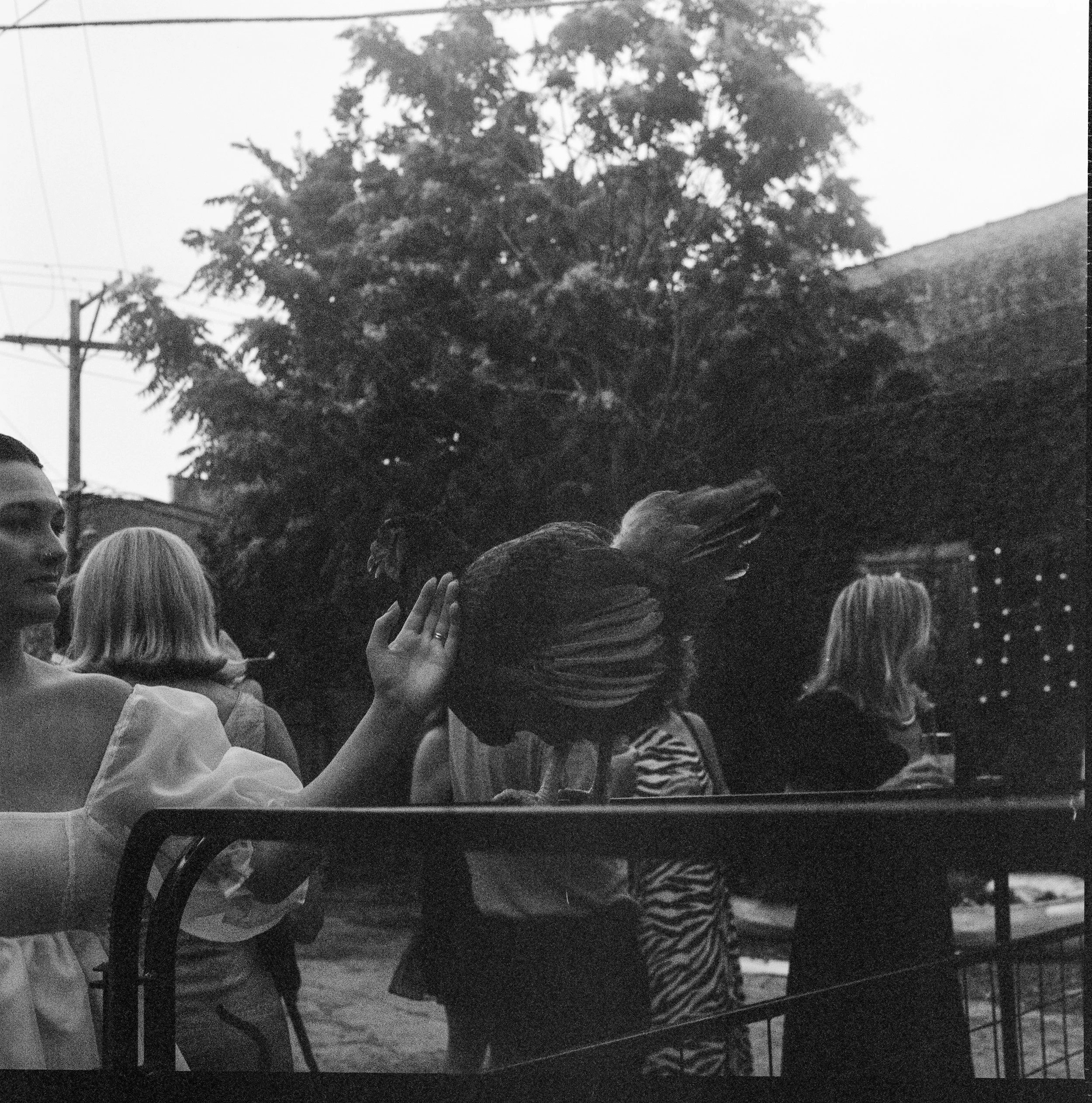 People gathered outdoors, some shielding their eyes from the sun, with a large tree and utility pole in the background, black-and-white photo.