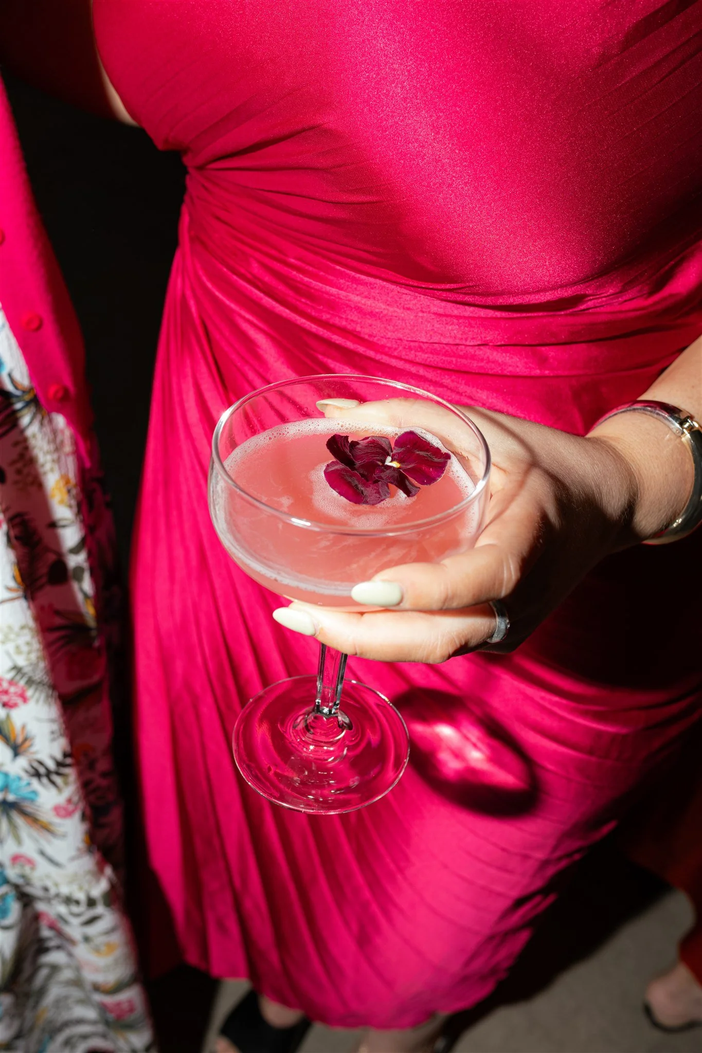 A woman in a vibrant pink dress holding a cocktail with flower garnish.
