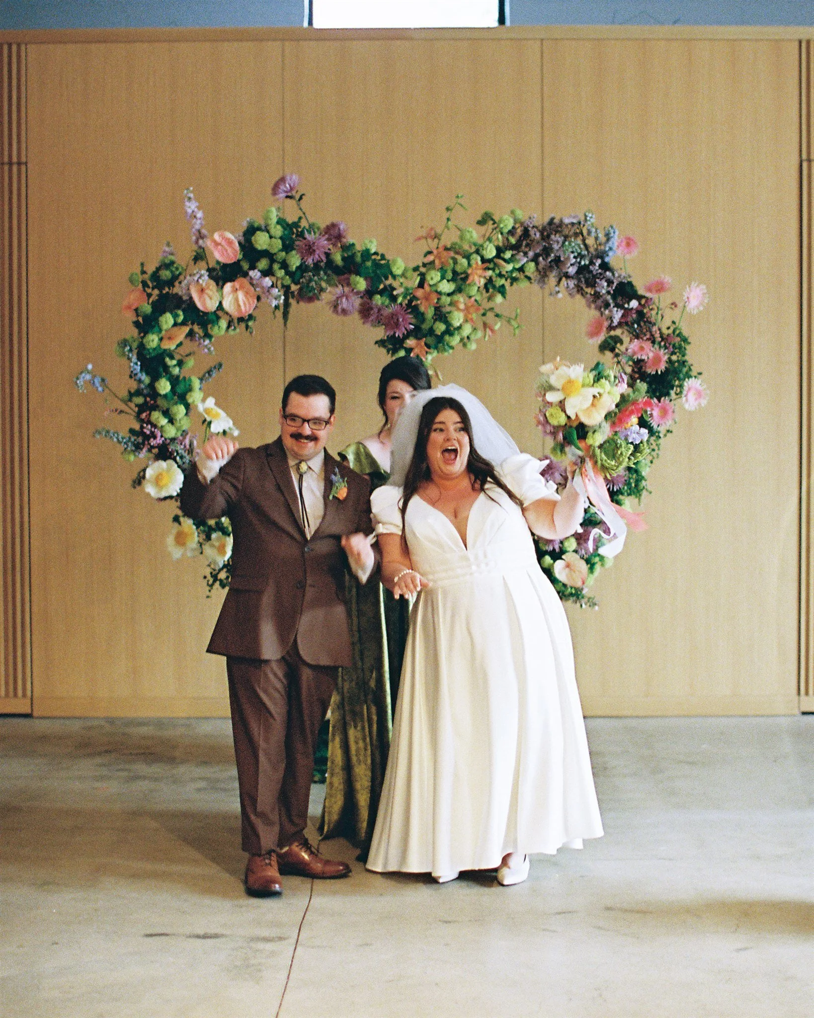 A bride and groom celebrating with an arch of colorful flowers in the background at a wedding reception.