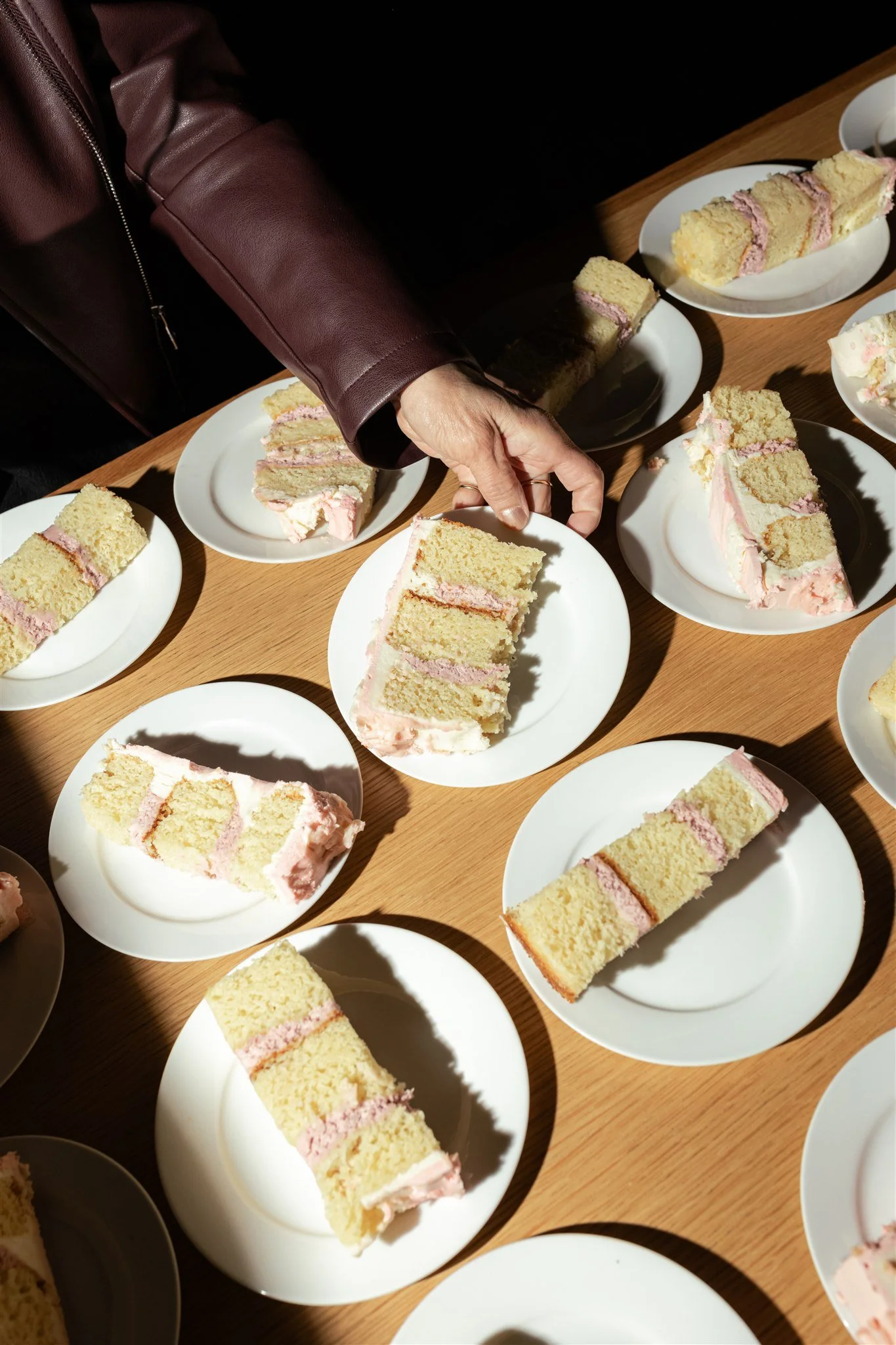 Multiple slices of cake with pink filling on white plates on a wooden table.