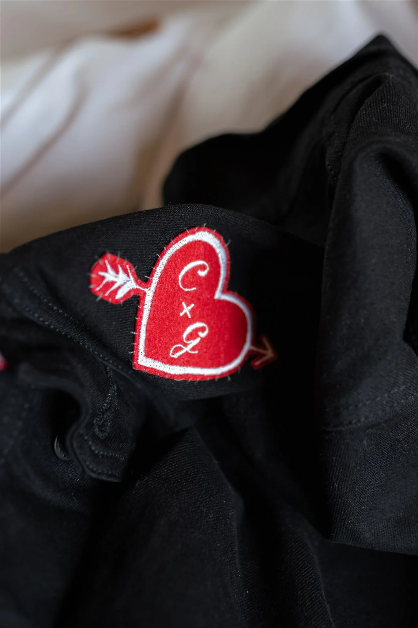 Close-up of a black garment with a red and white heart-shaped patch featuring a white arrow design.