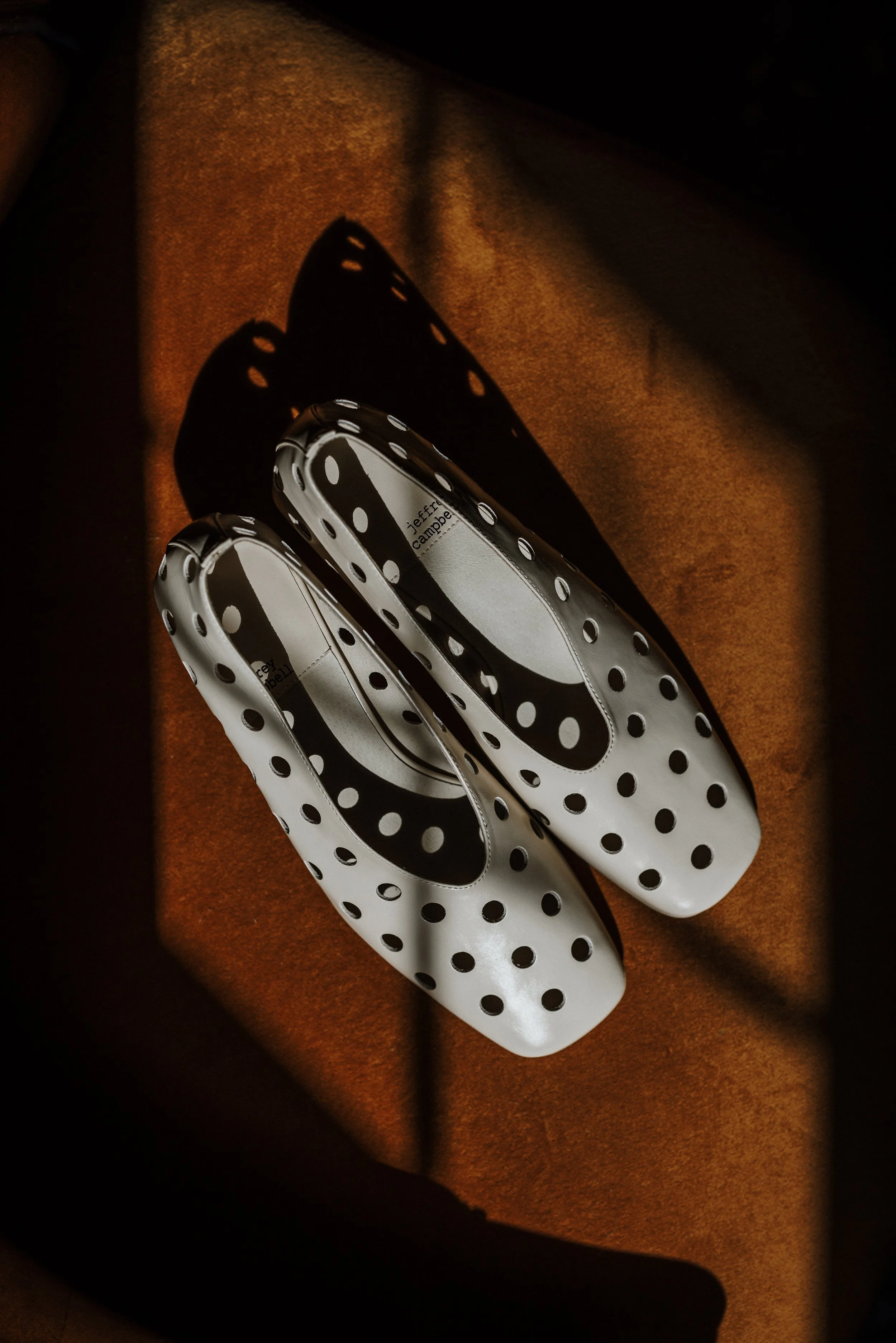 Polka dot shoes placed on an orange-brown surface, with a shadow cast nearby.