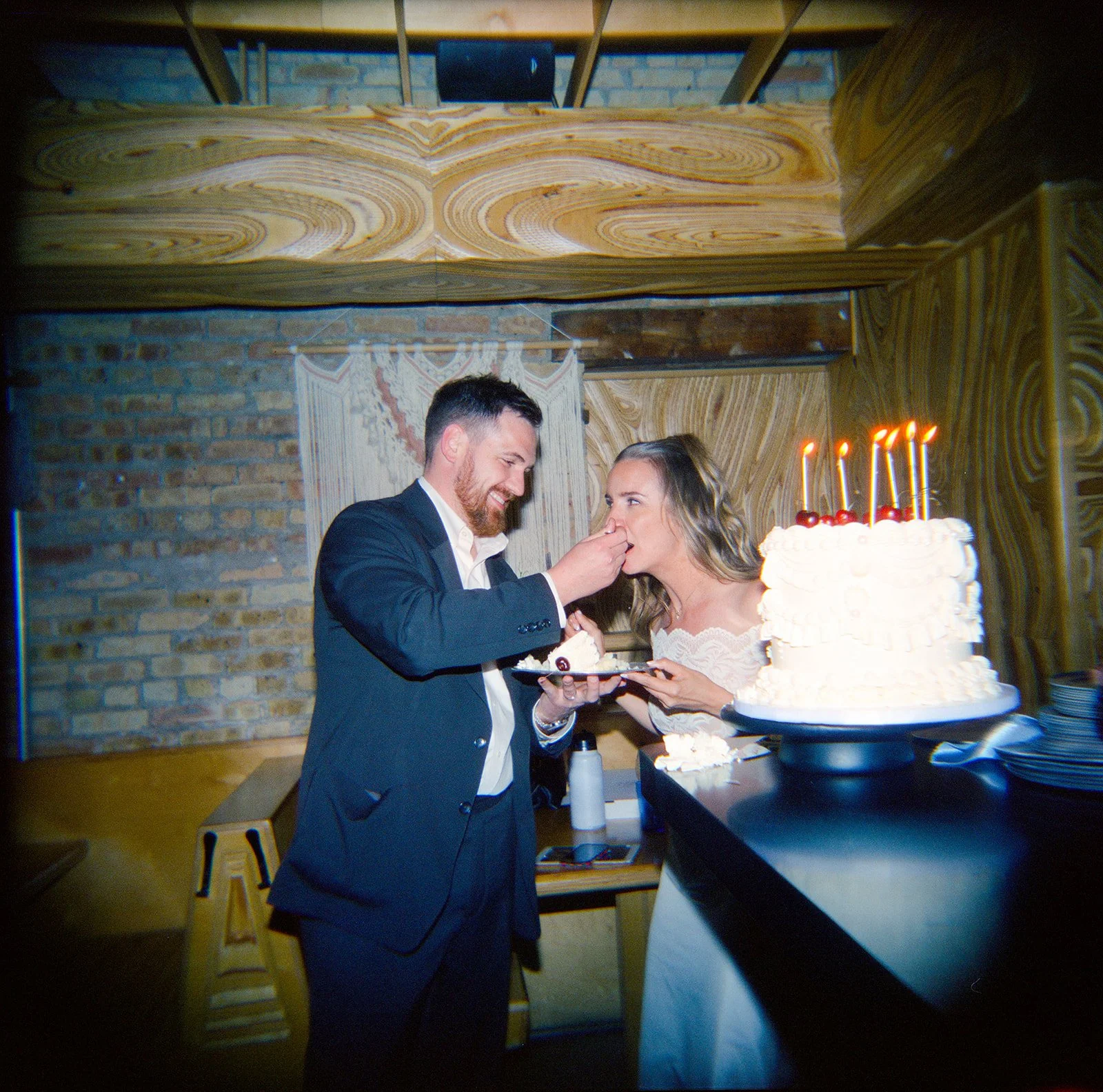 A man and woman celebrating a birthday with a large white cake with candles. The man is feeding the woman a piece of cake at a party.