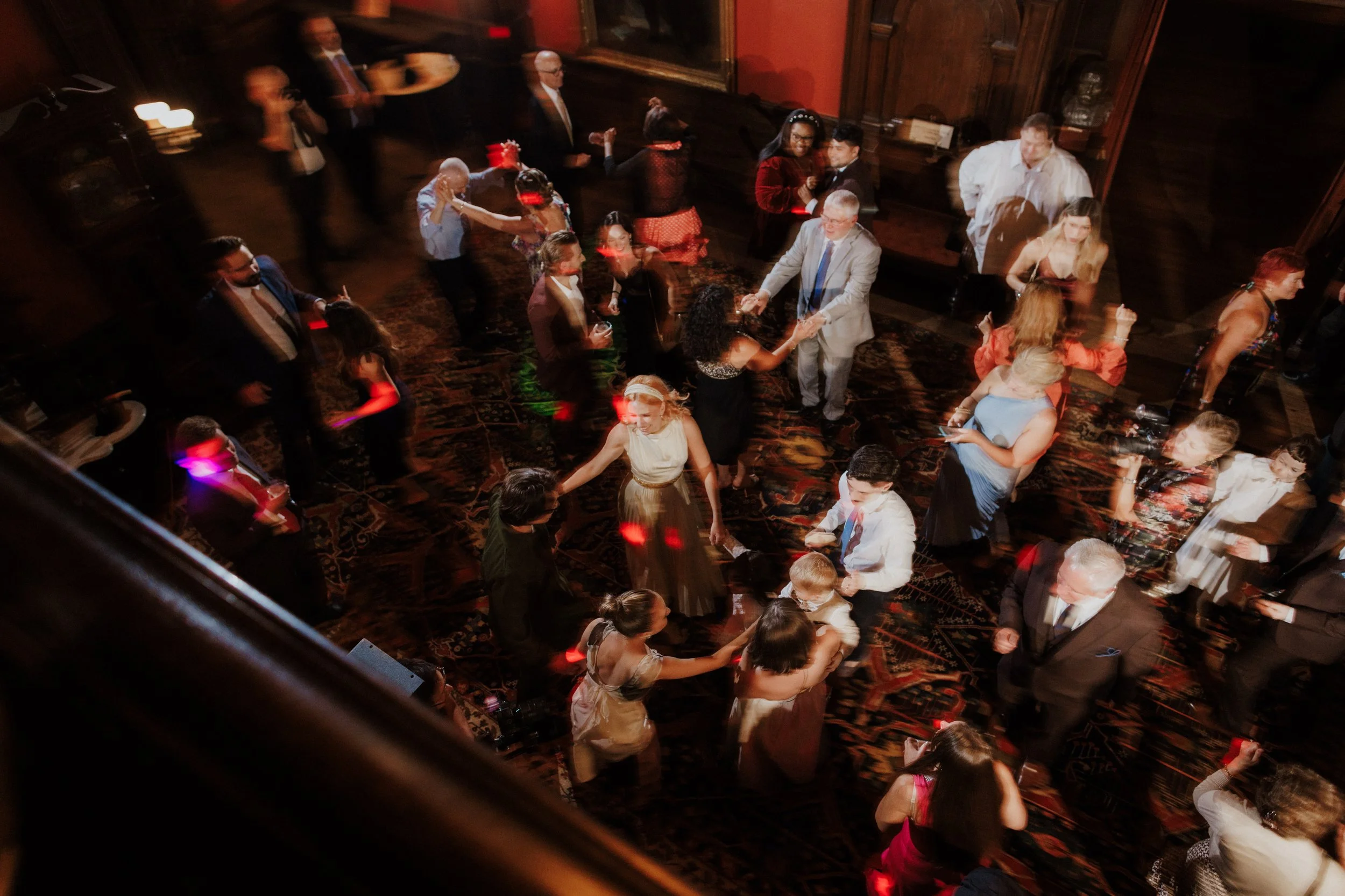 People dancing and socializing at a party in a formal setting with dim lighting and ornate decor.