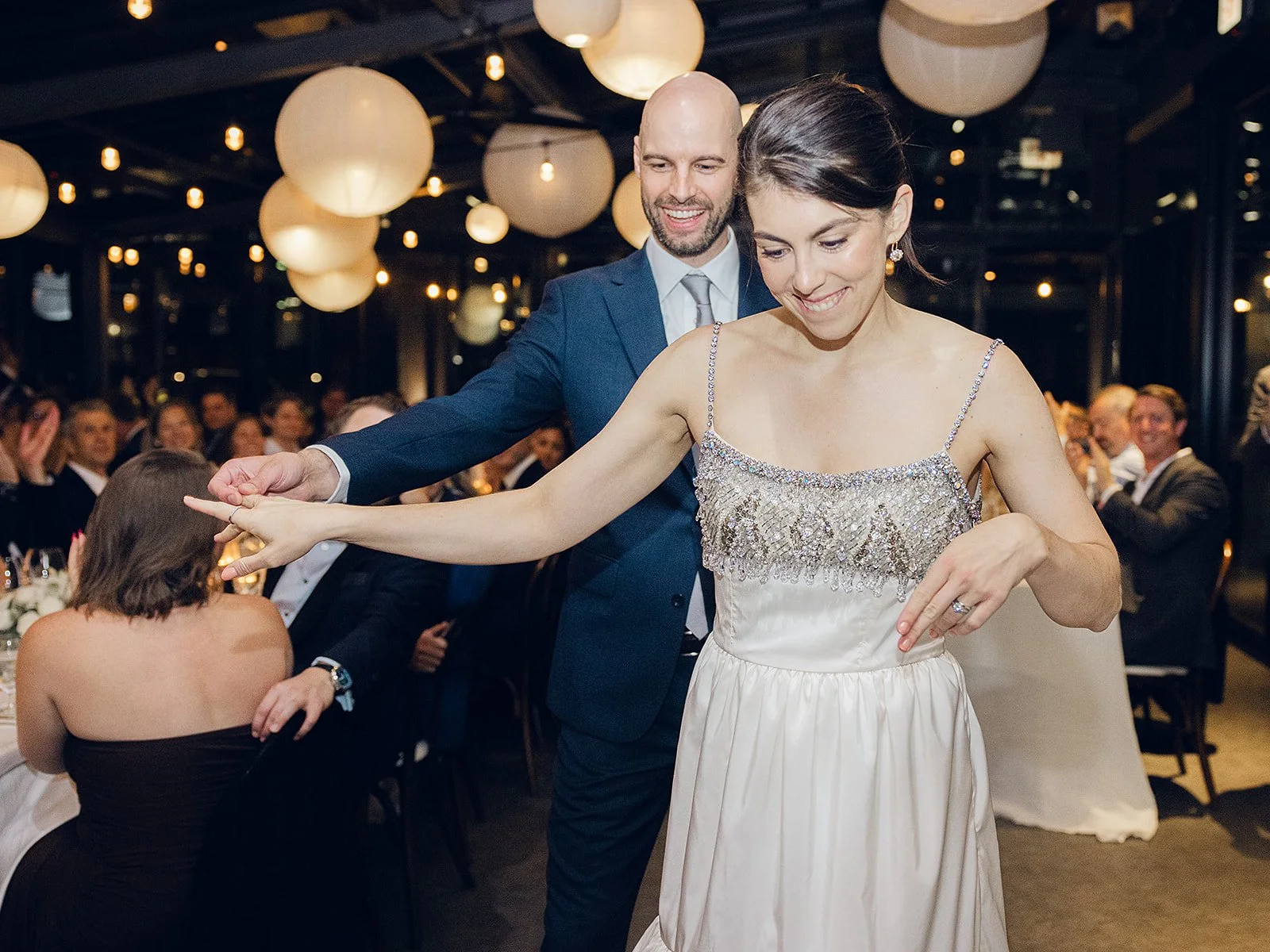 A wedding reception with a bride and groom dancing amid seated guests, decorated with round paper lanterns hanging from the ceiling.