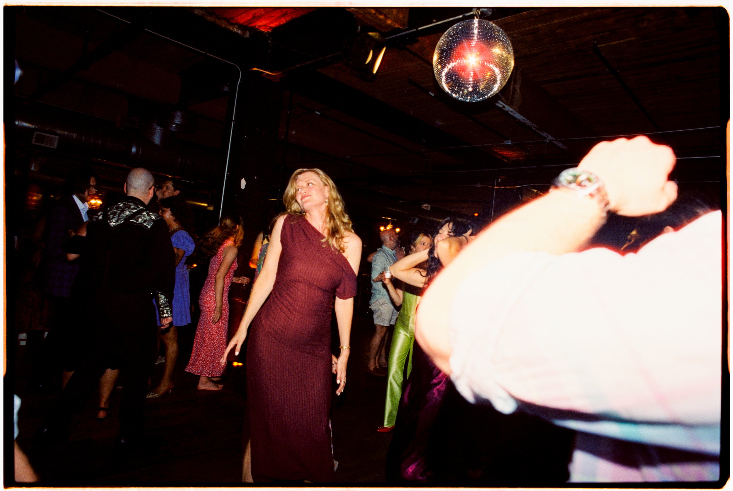 People dancing and socializing in a dimly lit nightclub with a disco ball hanging from the ceiling.