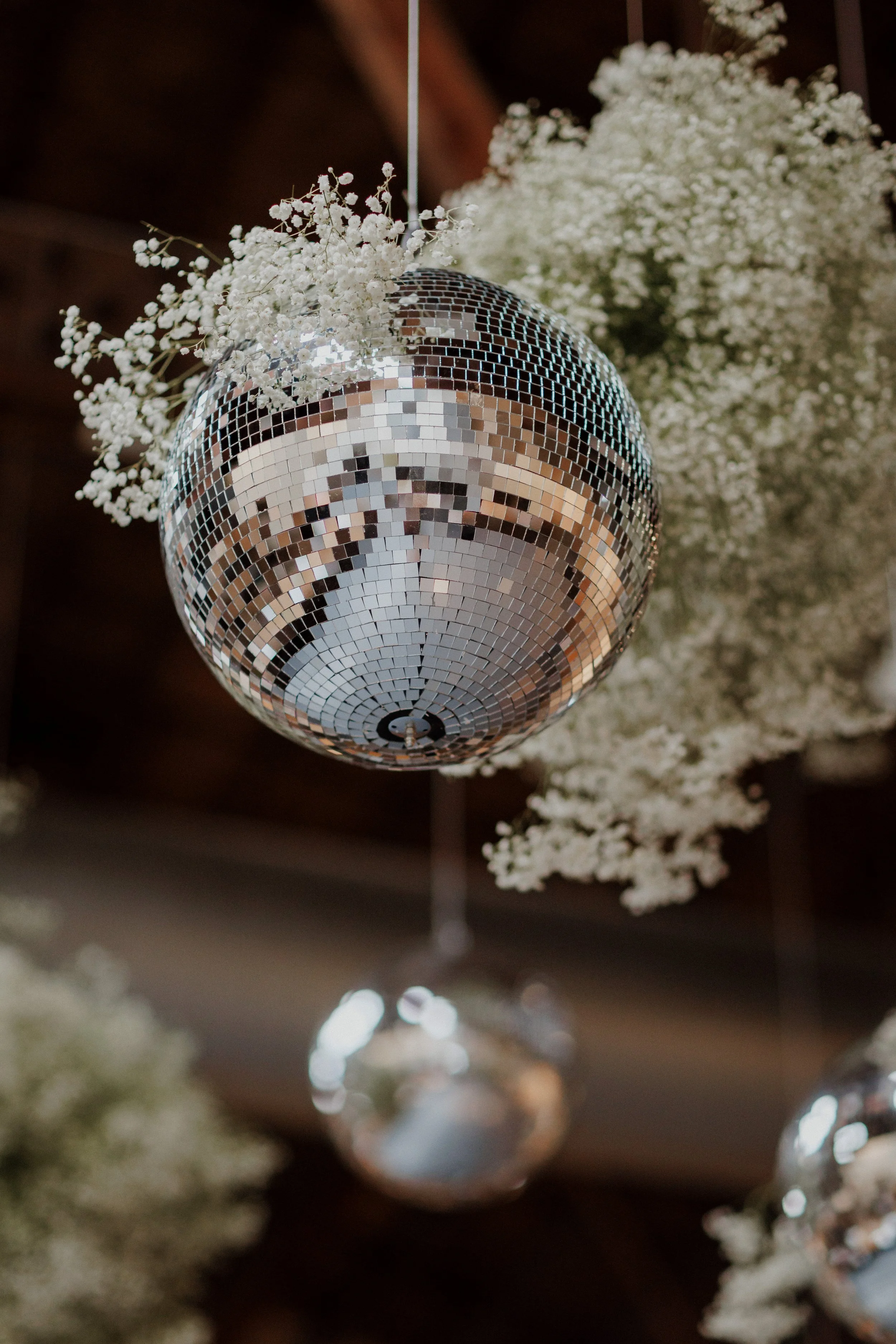 A disco ball hanging from the ceiling surrounded by white flowers.