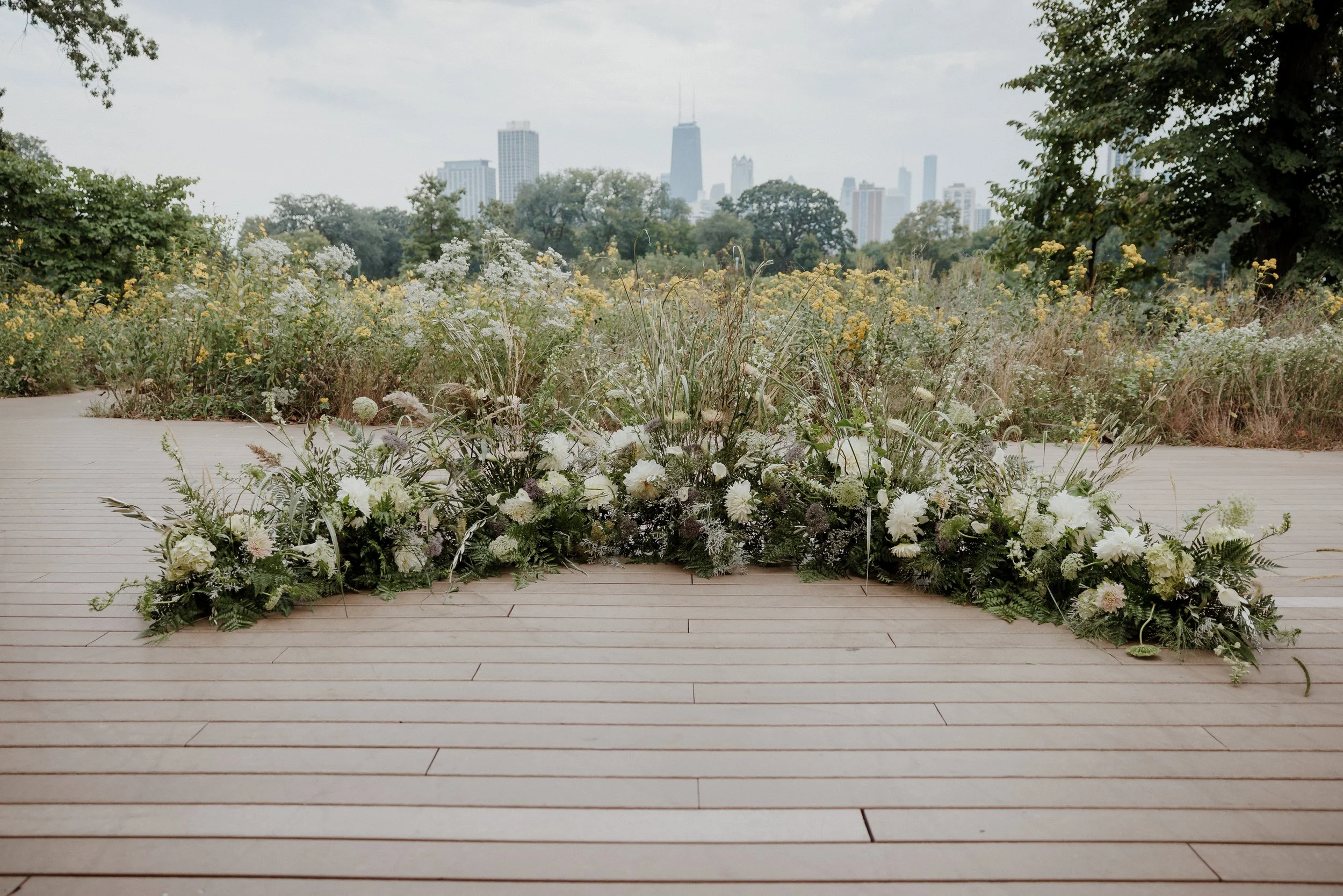 A floral arrangement on a wooden platform overlooking a park with trees and the Chicago skyline in the background.