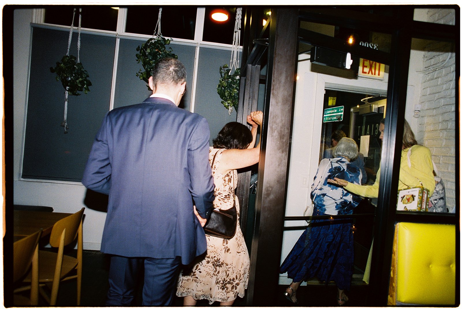 People entering a restaurant through a glass door, including a woman with a raised fist outside, with others walking inside.