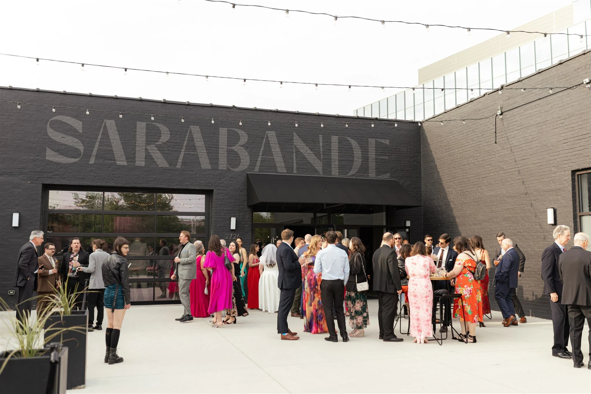 Group of people dressed in formal and colorful attire gathering outside a building at a social event or celebration.