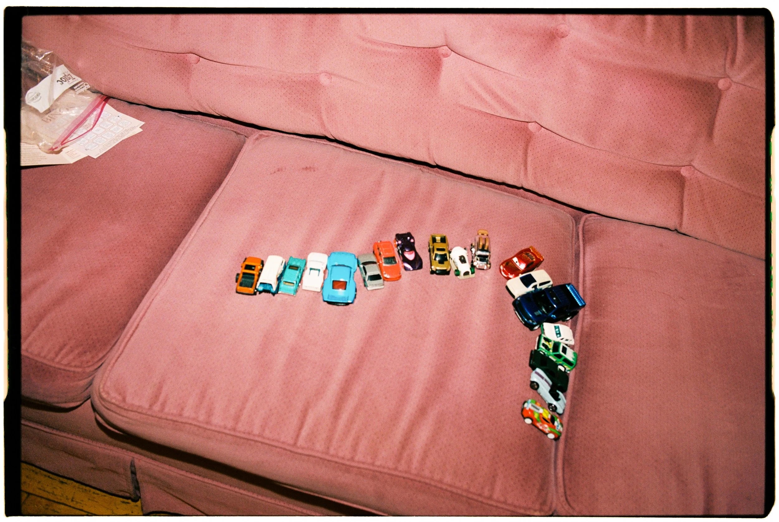 Small toy cars arranged in a line on a pink couch.