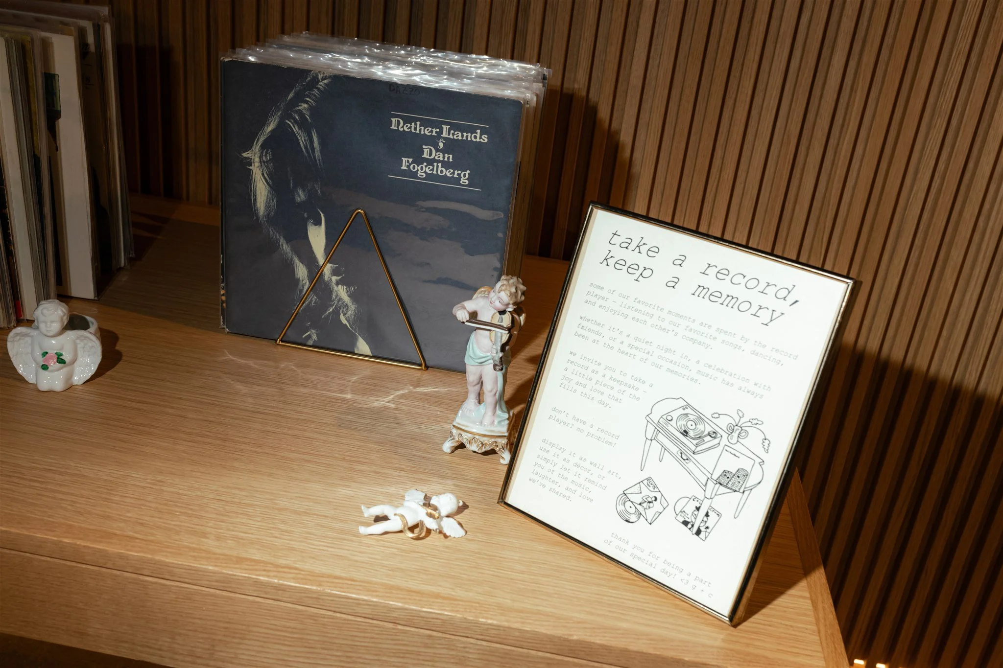 A wooden surface with a framed note, decorative angel figurines, a record album titled 'Nether Lands' by Dan Fogelberg, and a small angel figurine.
