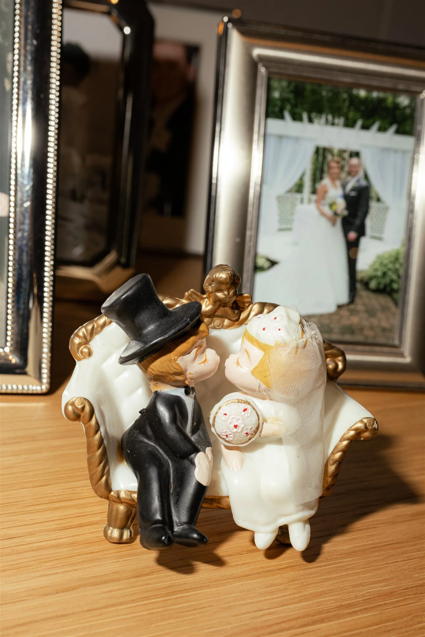 Decorative figurines of a bride and groom with a small dog, set in a basket, in front of a framed wedding photo and mirrors.