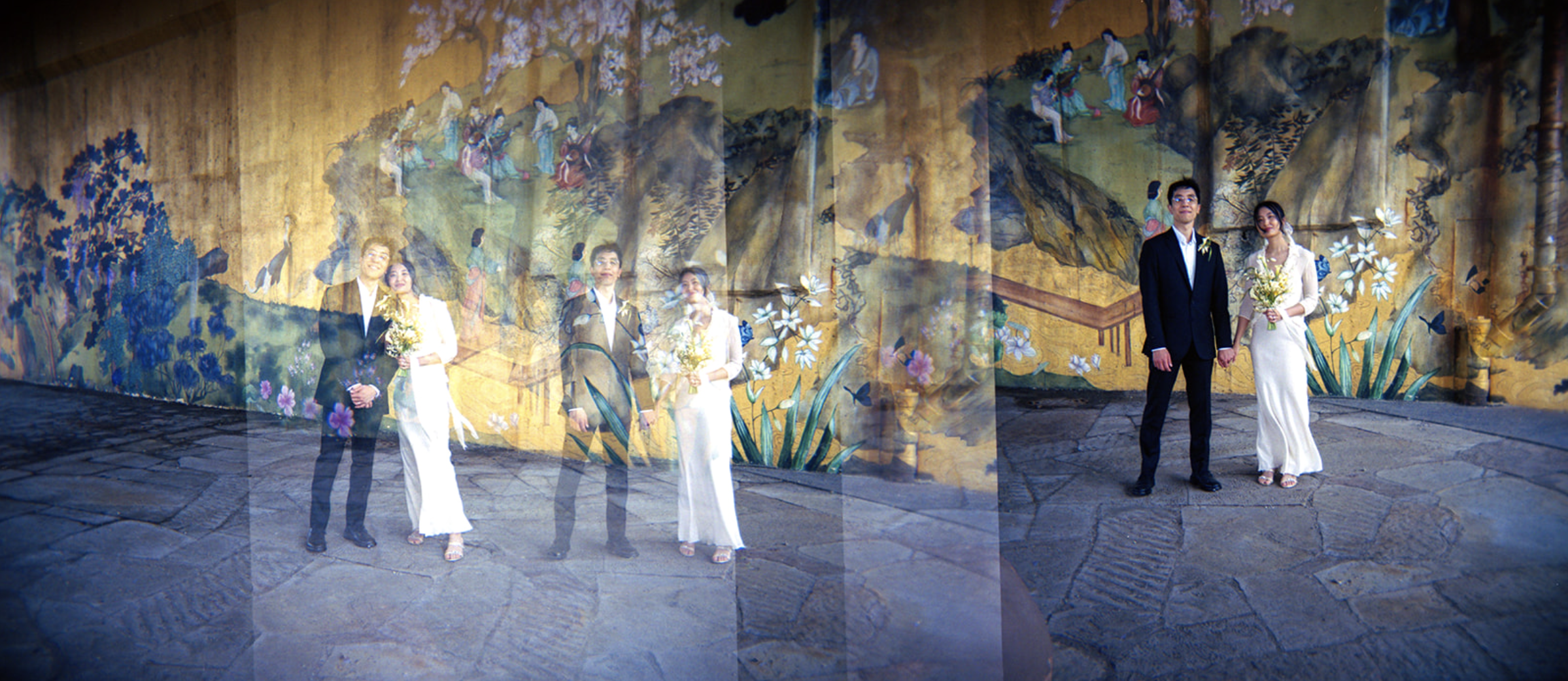 A wedding couple stands hand in hand in front of a painted mural with multiple reflections of themselves creating a layered visual effect.