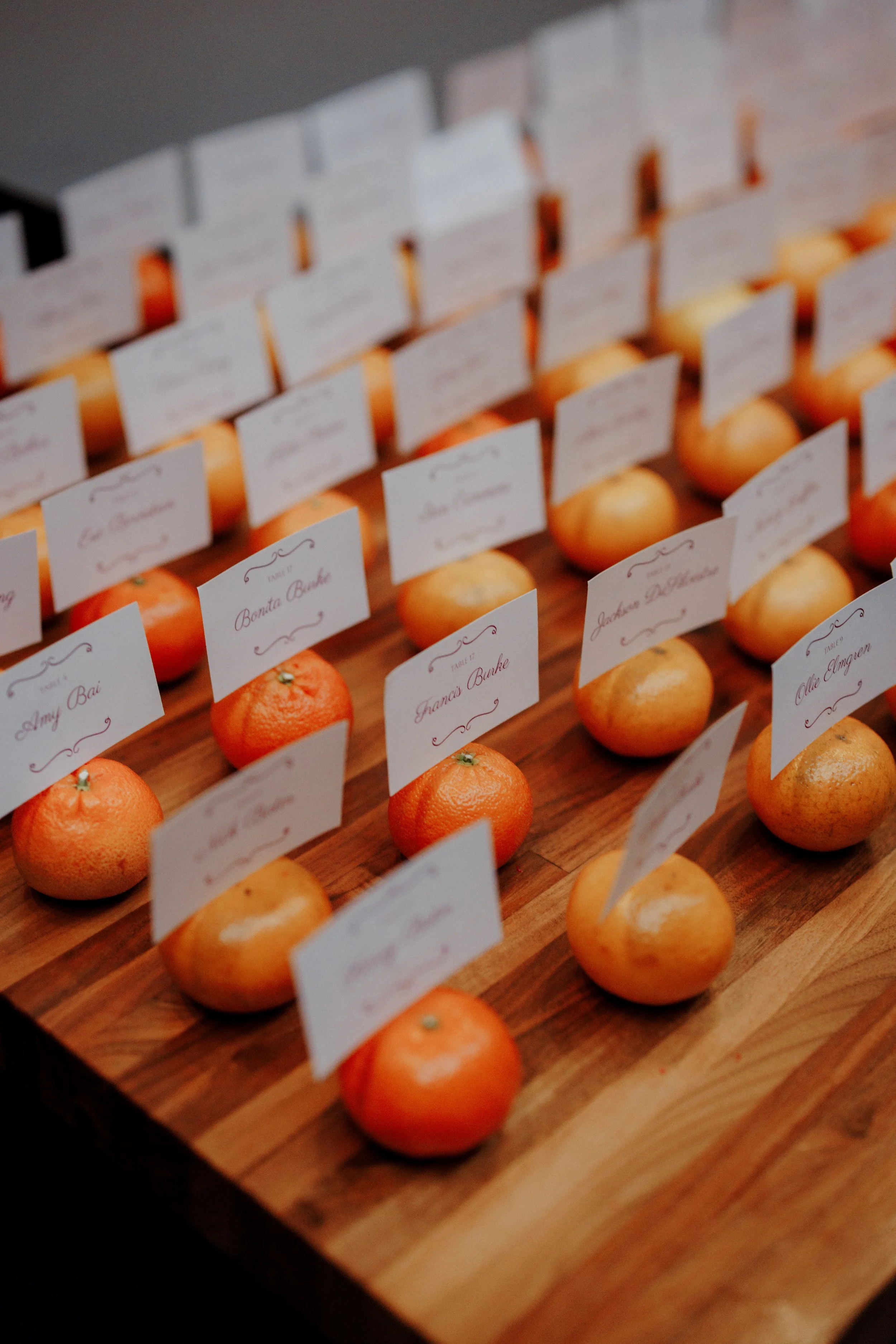 A wooden board with small oranges, each with a white card label with red cursive writing, organized in rows.