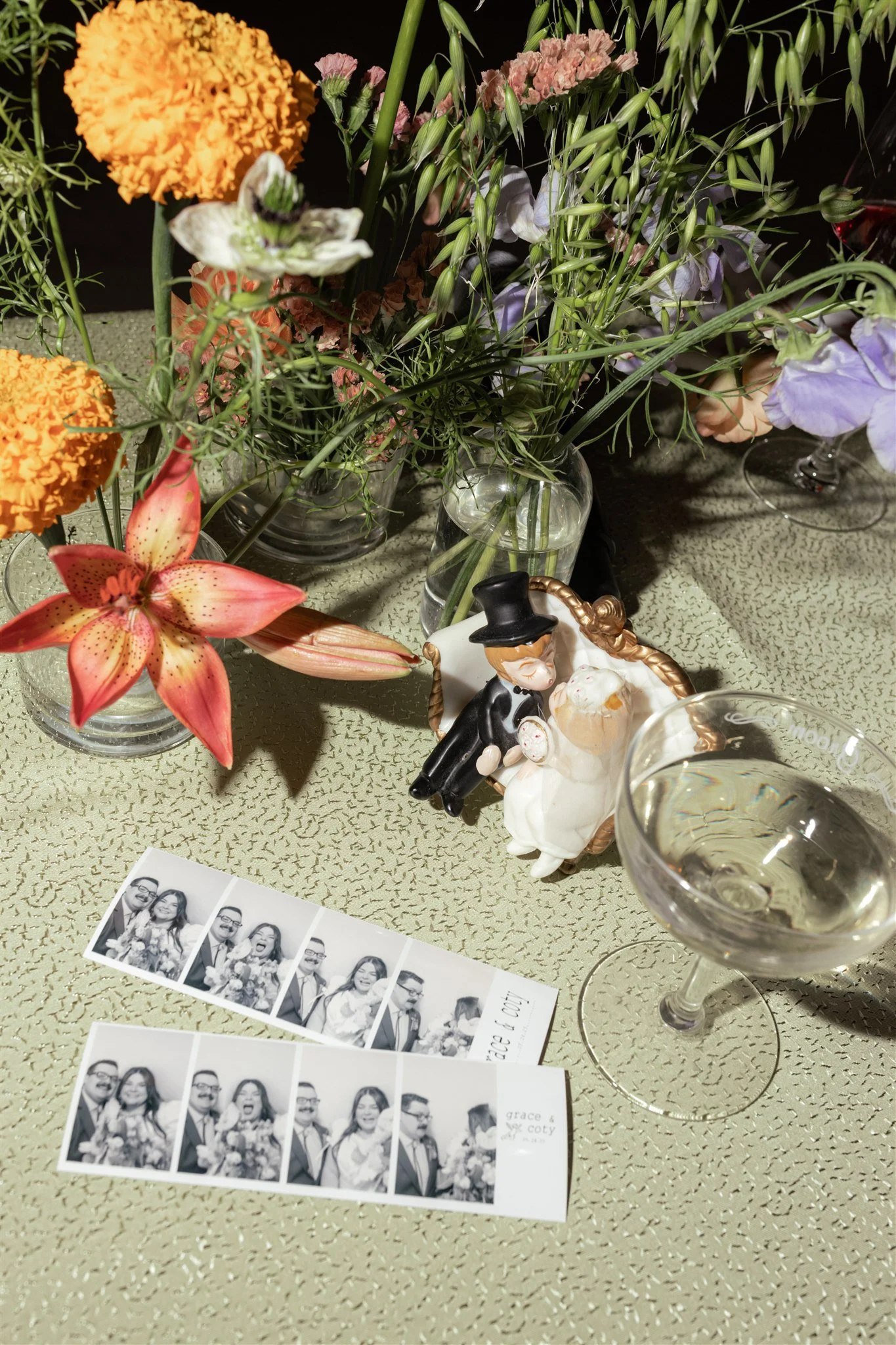 Arrangement of colorful flowers and a photo booth strip on a table, with a glass of white wine in the foreground.