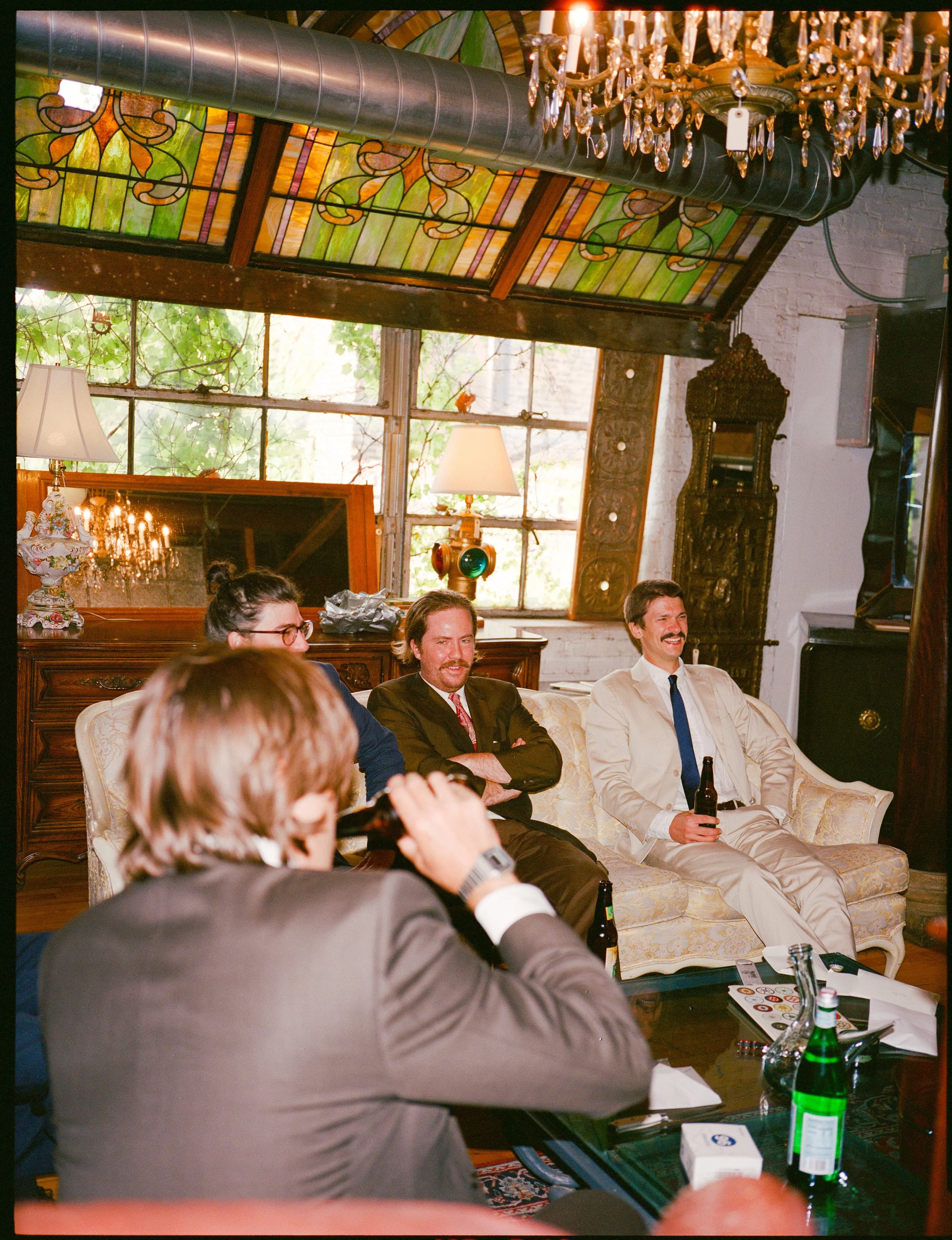 People sitting on a vintage couch in a room with stained glass windows and brass chandelier, participating in a social gathering or meeting.