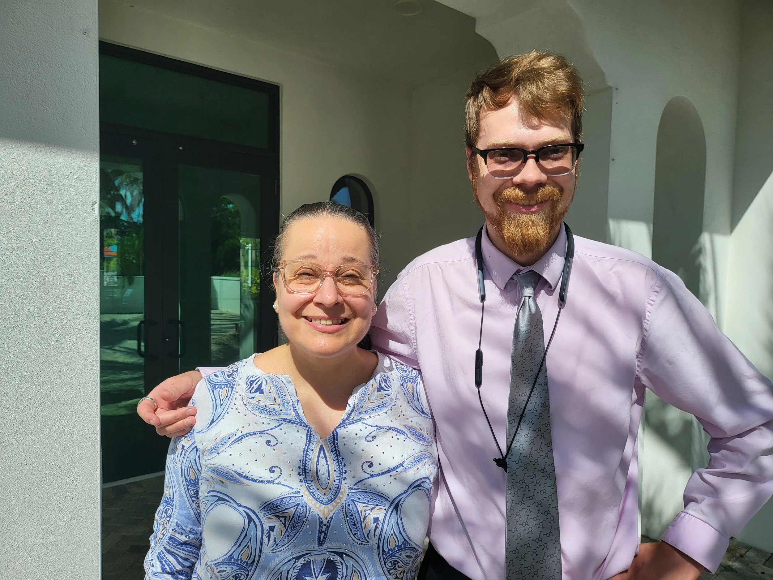 Blaise Jorgensen, candidate for Washoe County Public Administrator, standing next to a woman, outside a building with glass doors and white walls.