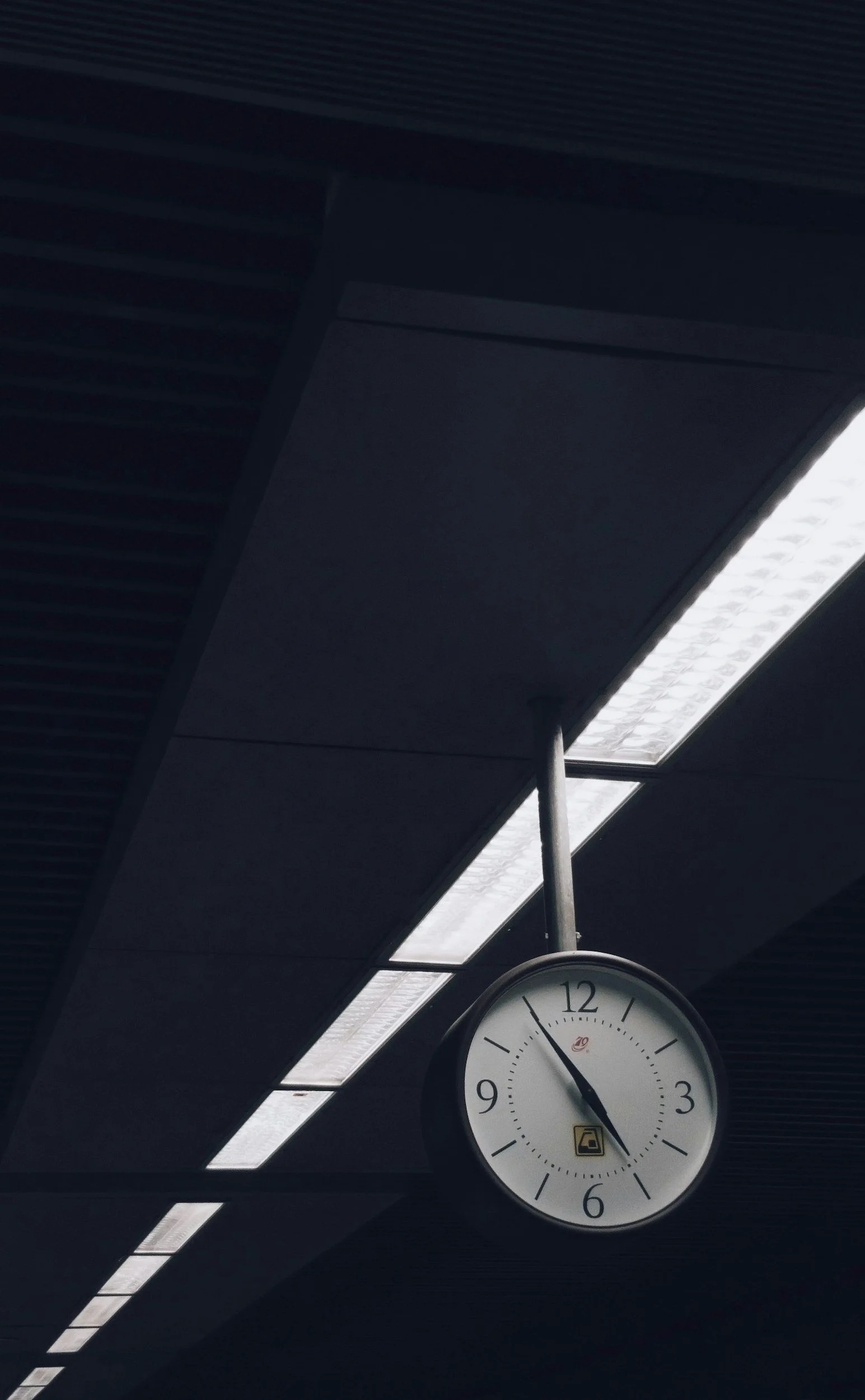 An indoor clock showing 4:56 hanging from the ceiling near fluorescent lights.