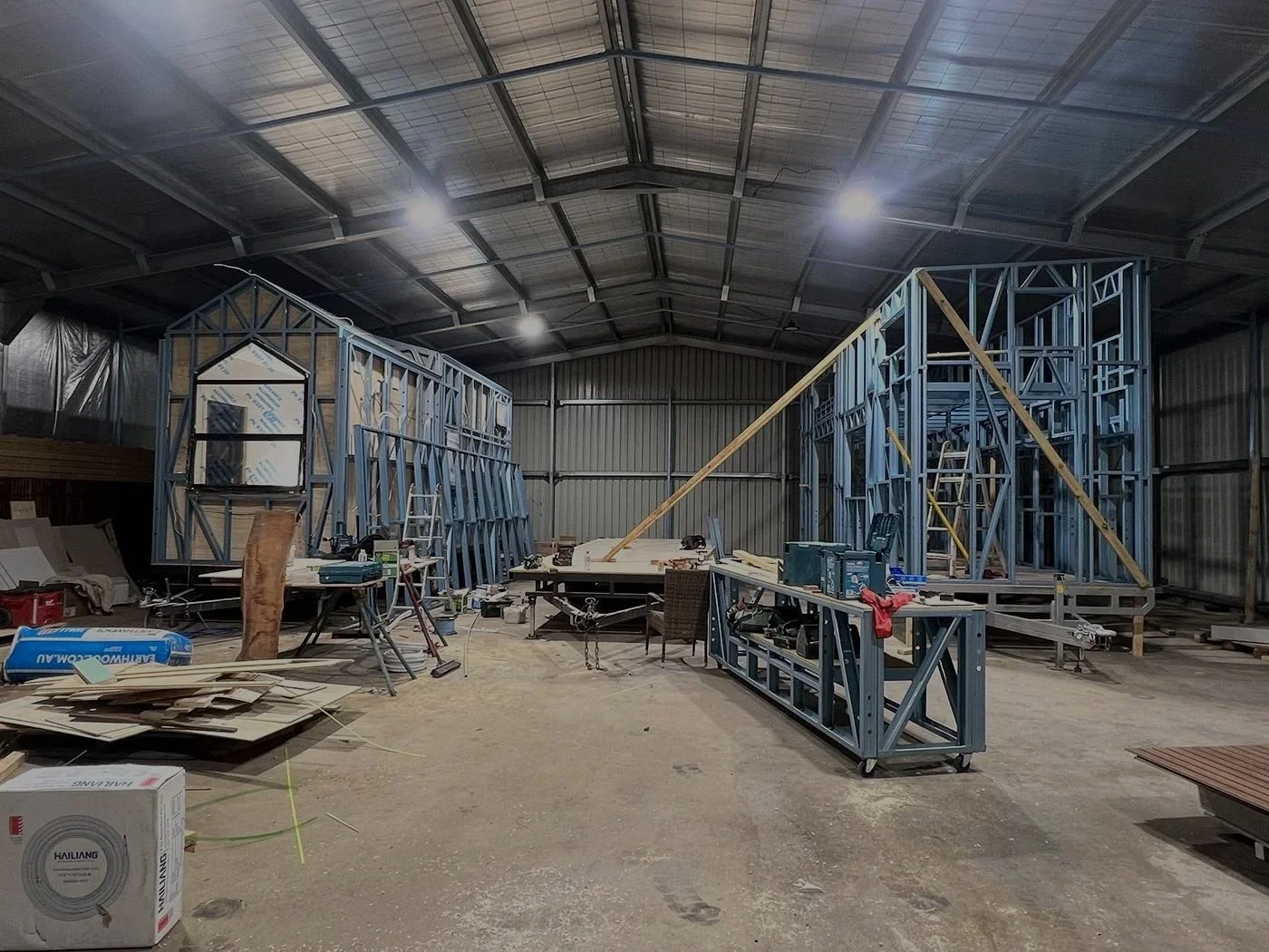 Interior of a metal Workshop under construction with steel frames, ladders, work tables, and construction tools.