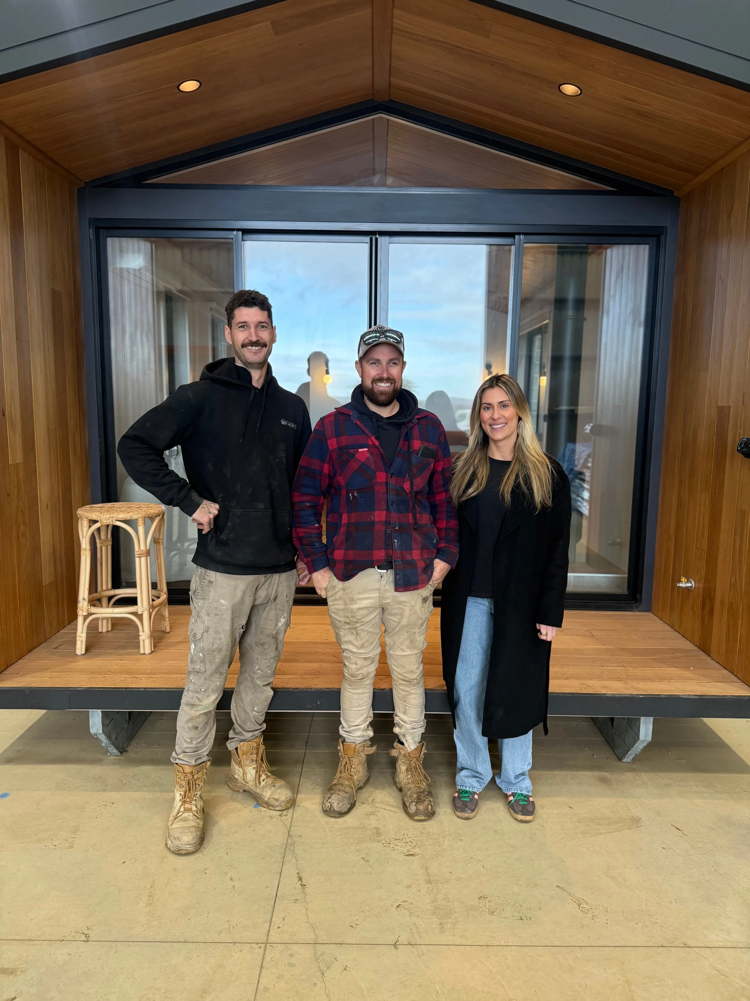 Iconic Tiny Home Founders standing, smiling for the photo in front of a tiny home. Two men are wearing work boots, and one woman is dressed casually.