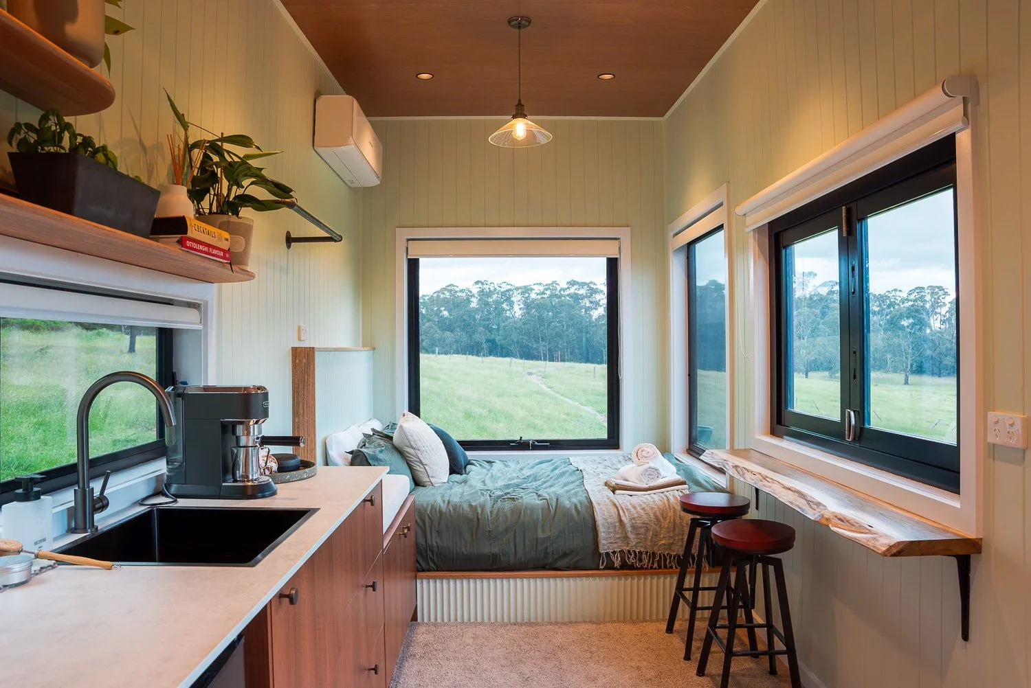 Small studio room with kitchen area and a bed near the large windows overlooking a green landscape.