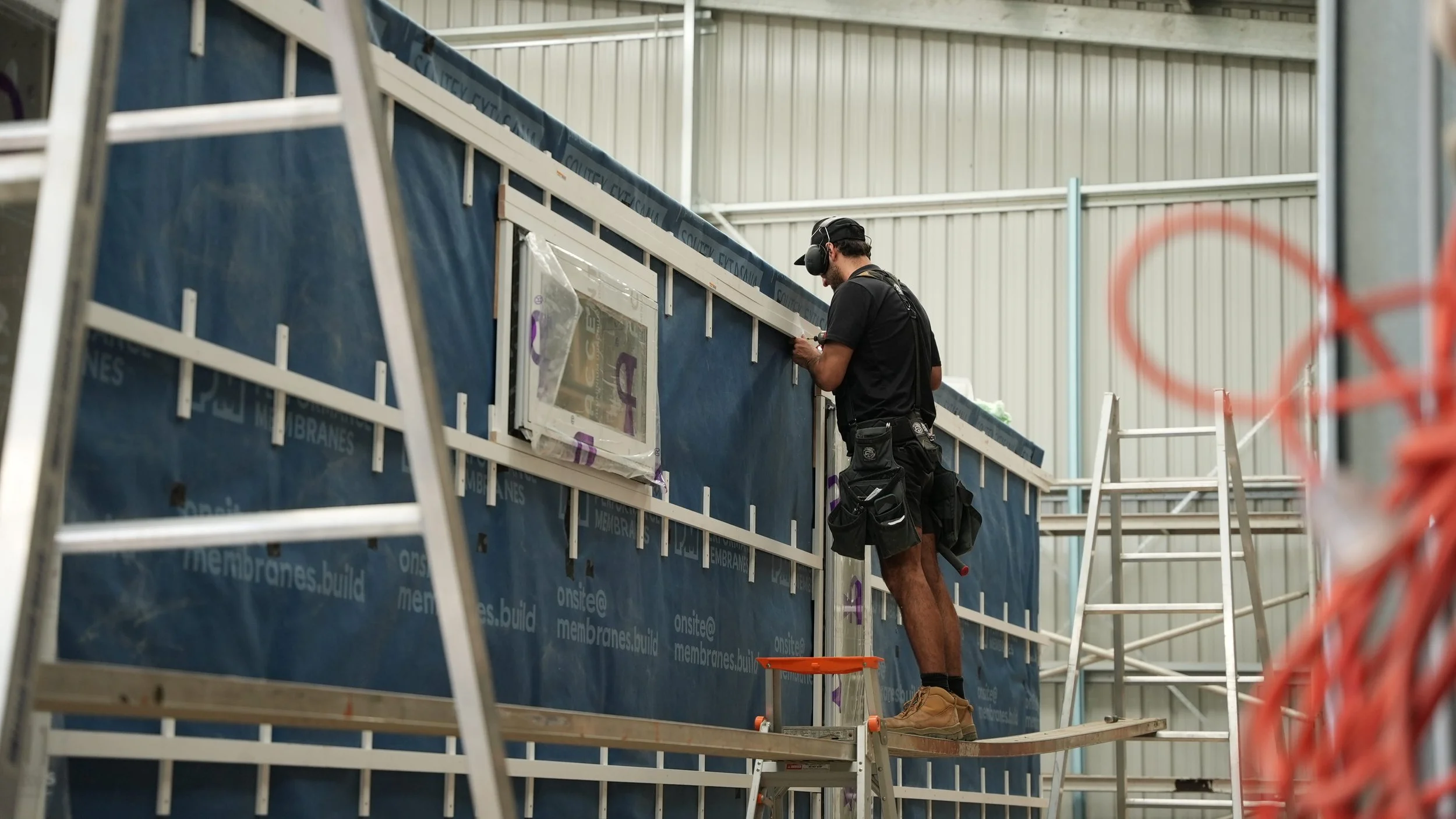 Interior of a metal Workshop under construction with steel frames, ladders, work tables, and construction tools.
