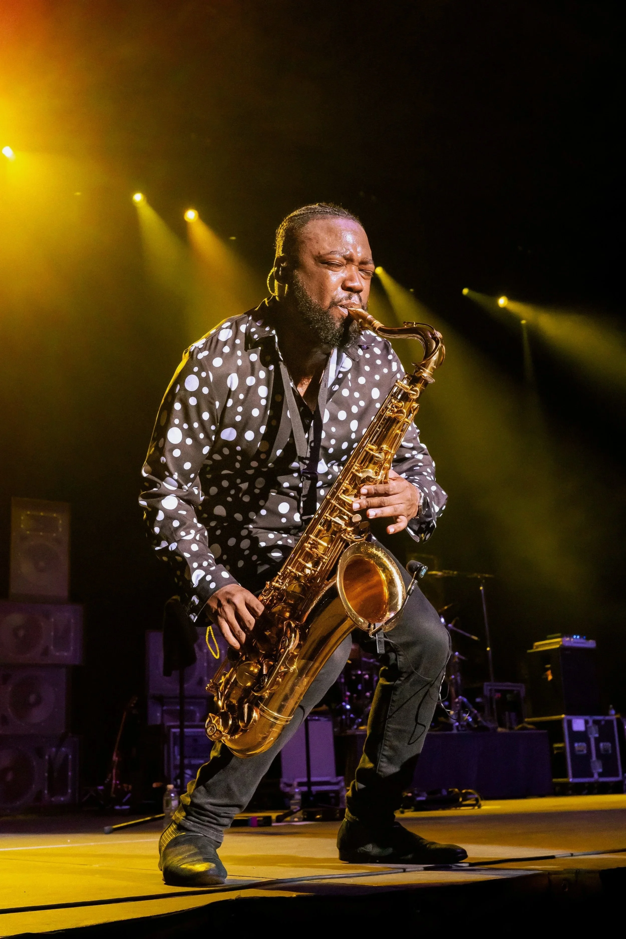 A man playing a saxophone on stage with yellow stage lighting.