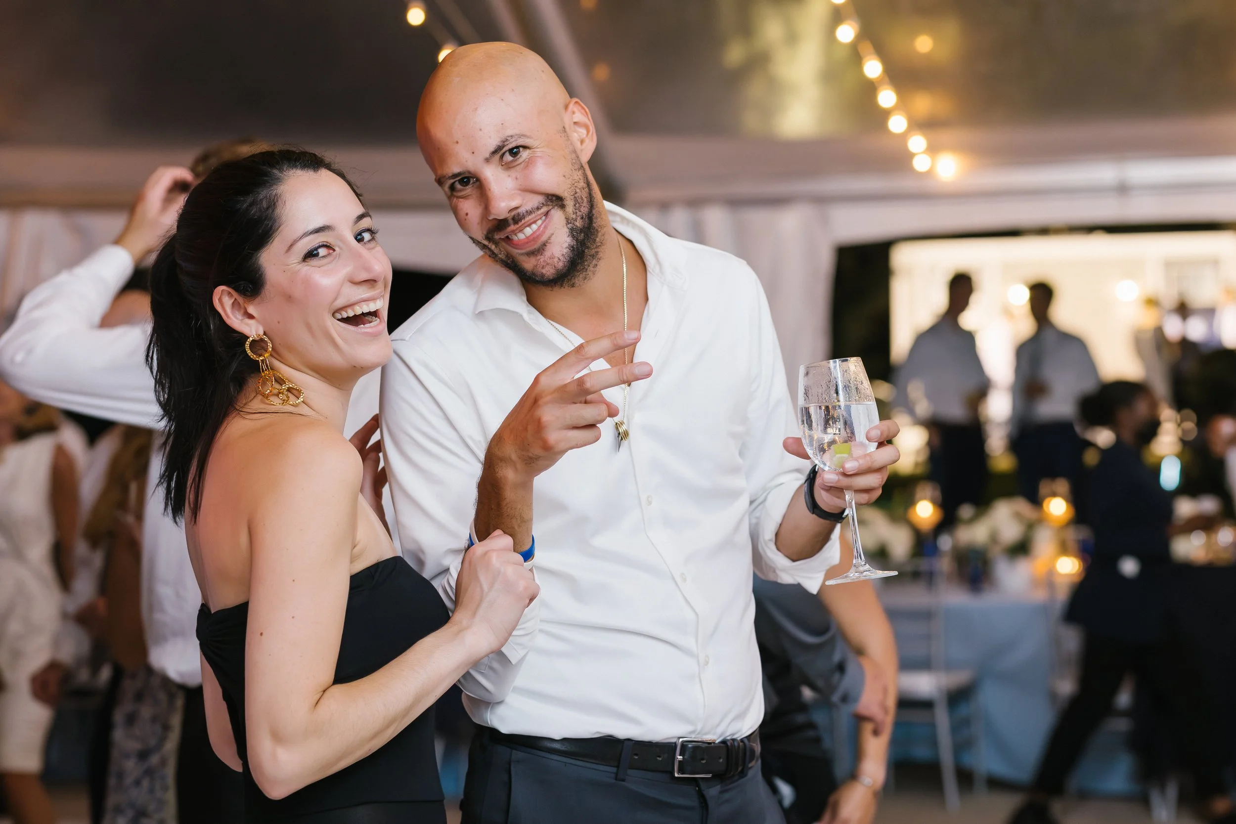 A man and a woman smiling and posing together at a social event or party, with the man holding a glass of water with lemon slices in it.