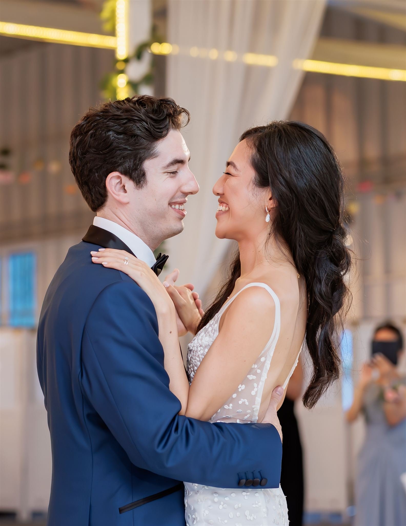 A couple in wedding attire sharing a dance and smiling at each other in a decorated venue.