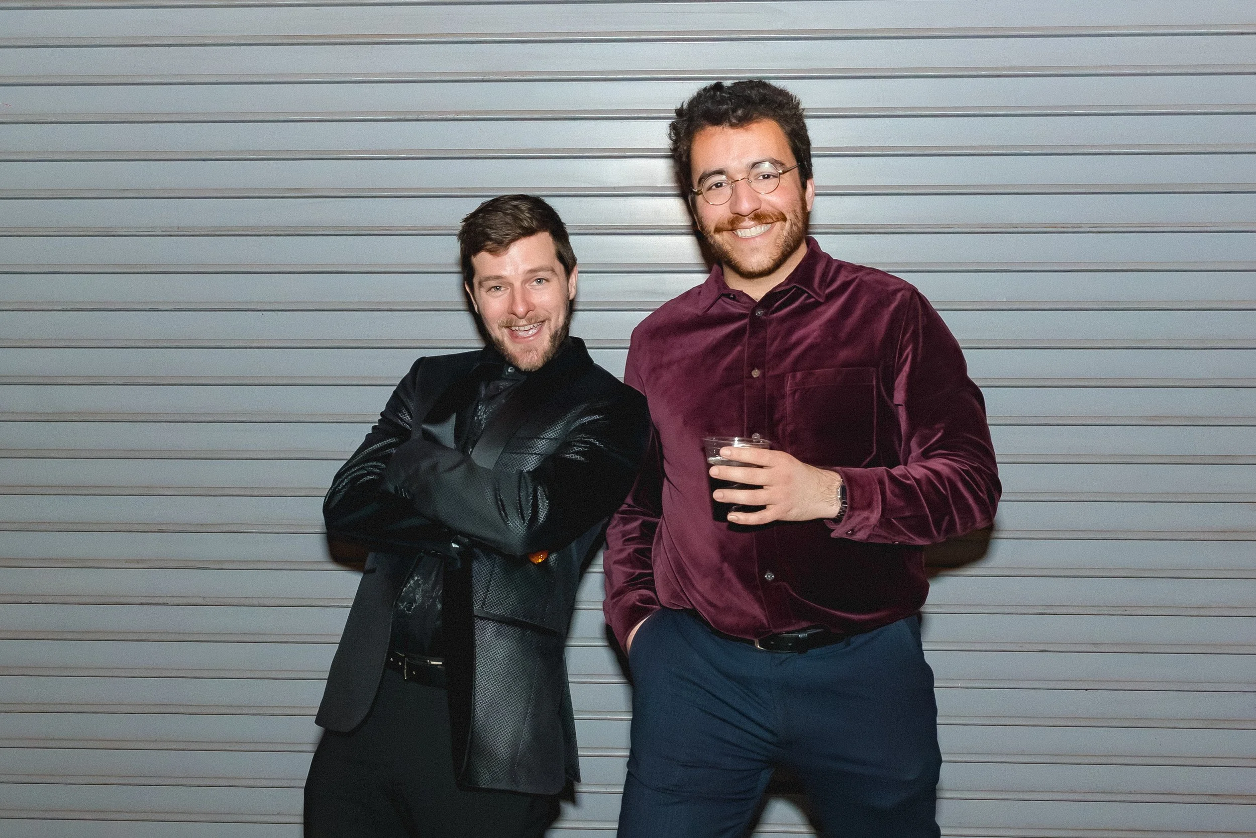 Two men smiling and posing in front of a metallic roller shutter.