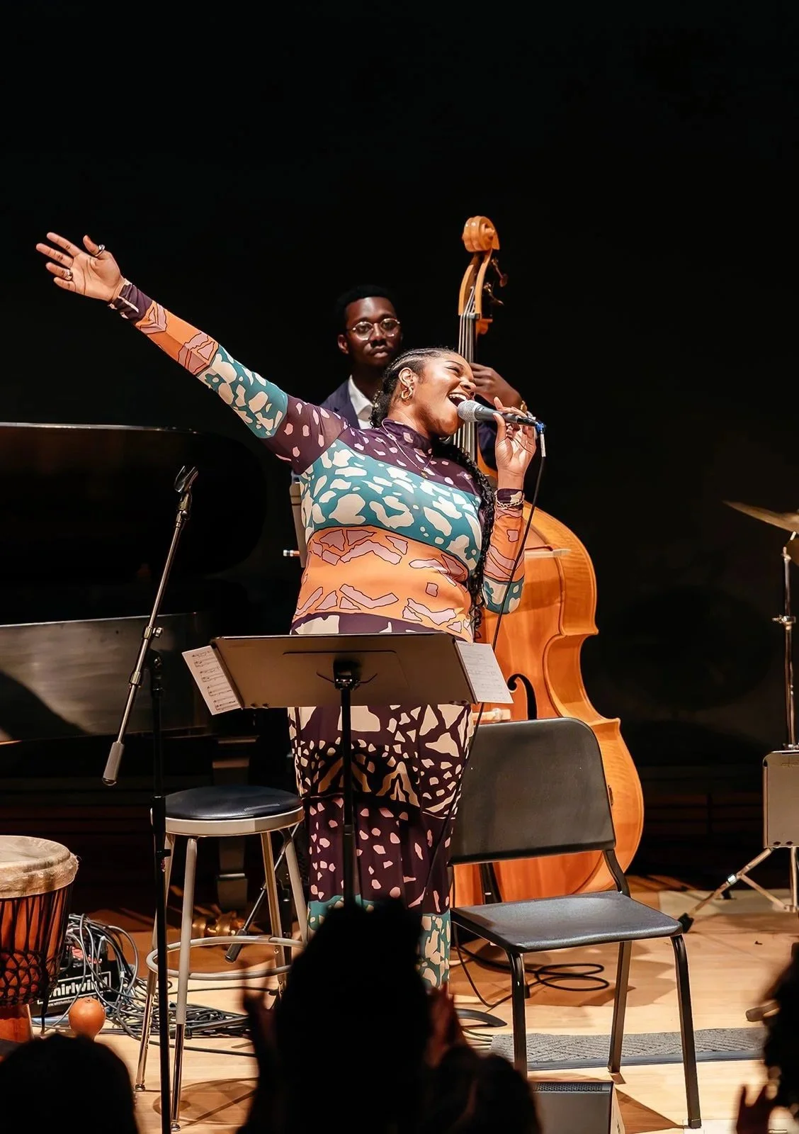 Jazz performance featuring a female singer with her arm raised and a male double bass player in the background on stage.