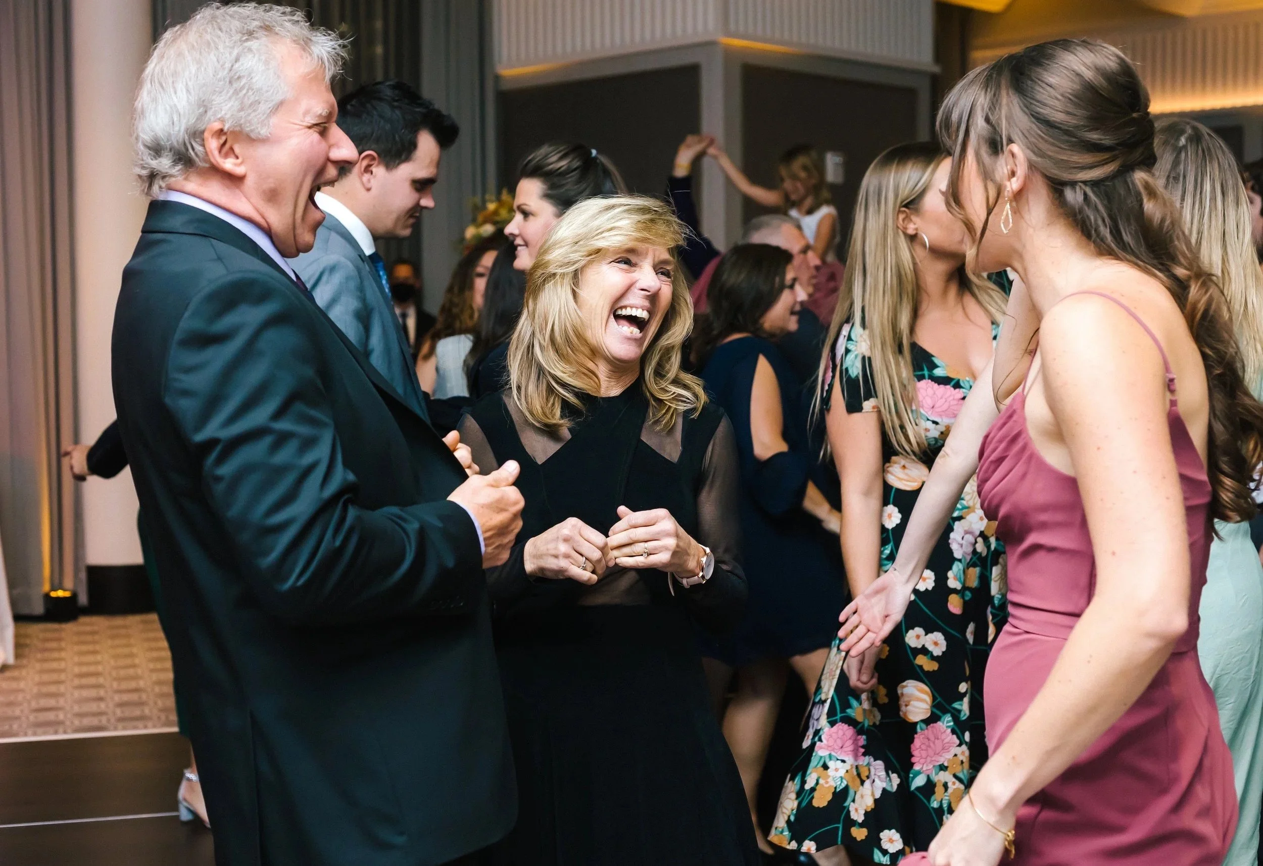 People at a social event laughing and talking in a lively atmosphere, dressed in formal and semi-formal attire.