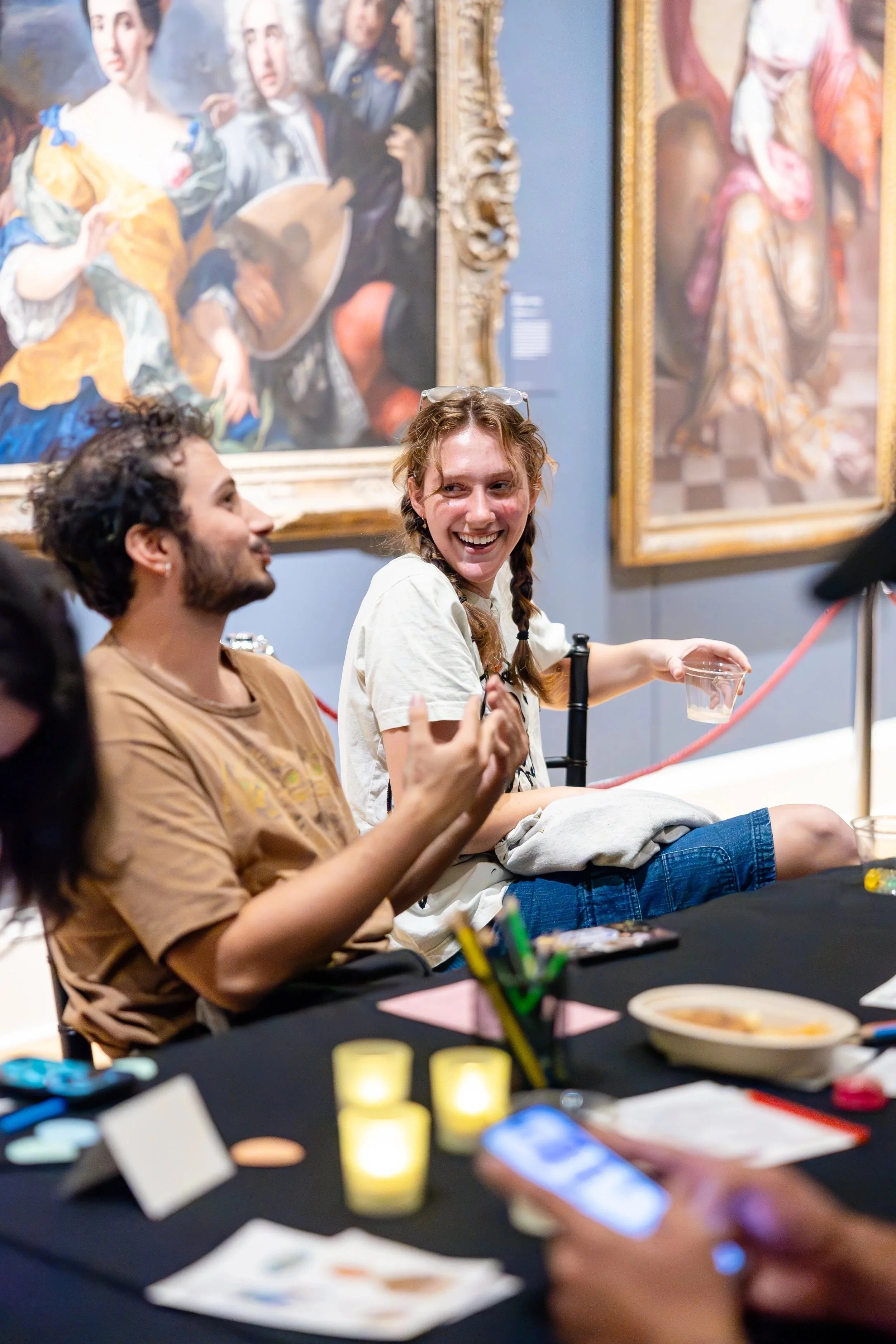 People sitting at a table in an art gallery, laughing and talking, with framed paintings on the wall behind them.