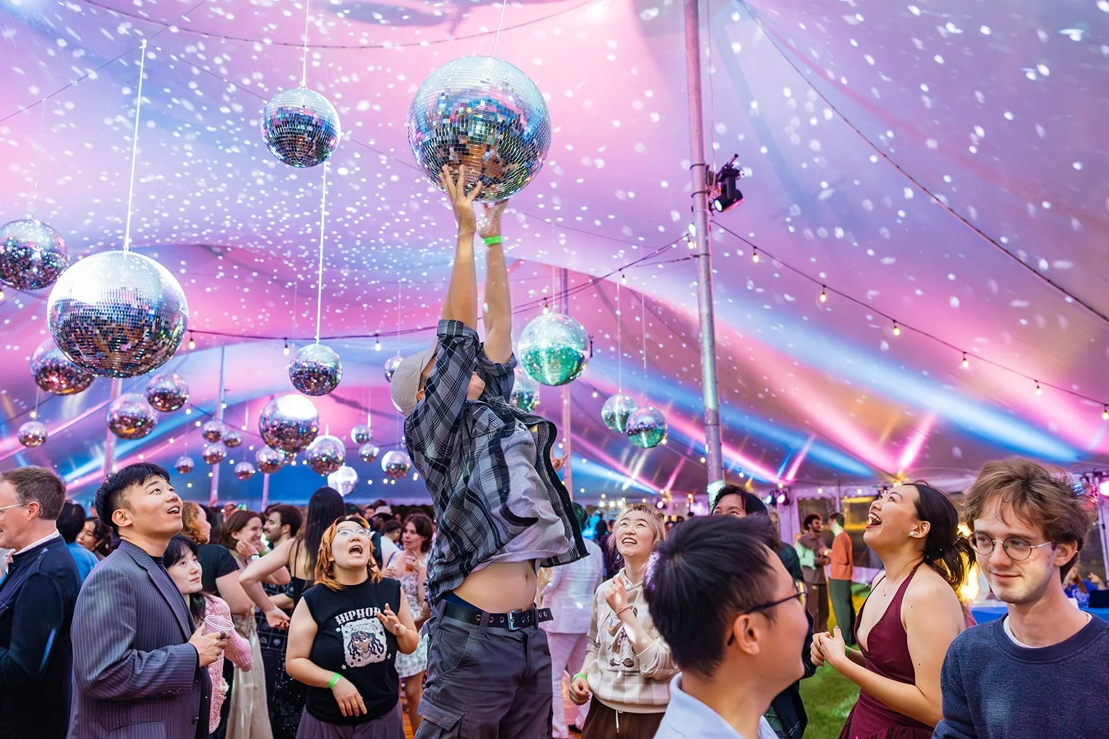 People dancing and celebrating under a tent with disco balls and colorful lights.